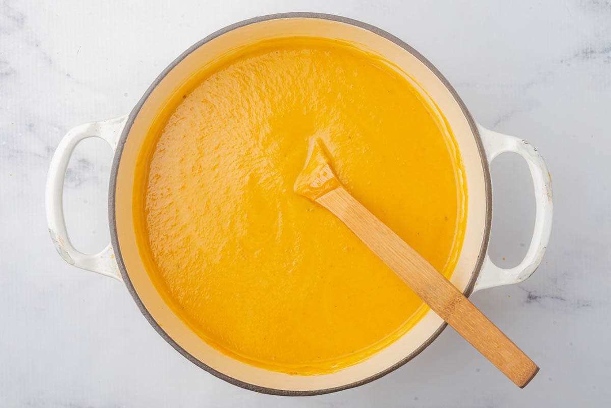 Smooth pumpkin soup in pot with wooden spoon.