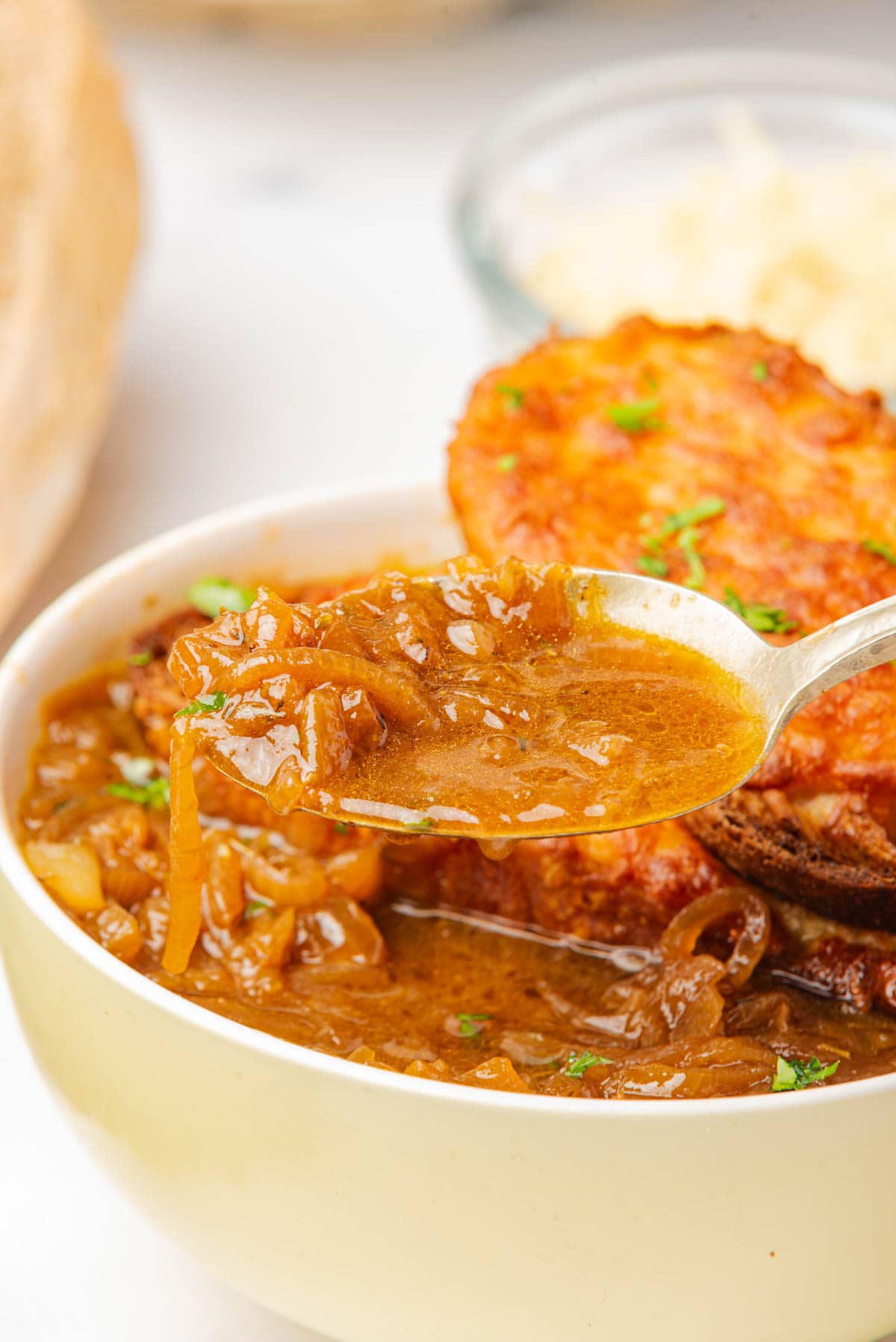 Bowl of French onion soup with a spoonful in front.