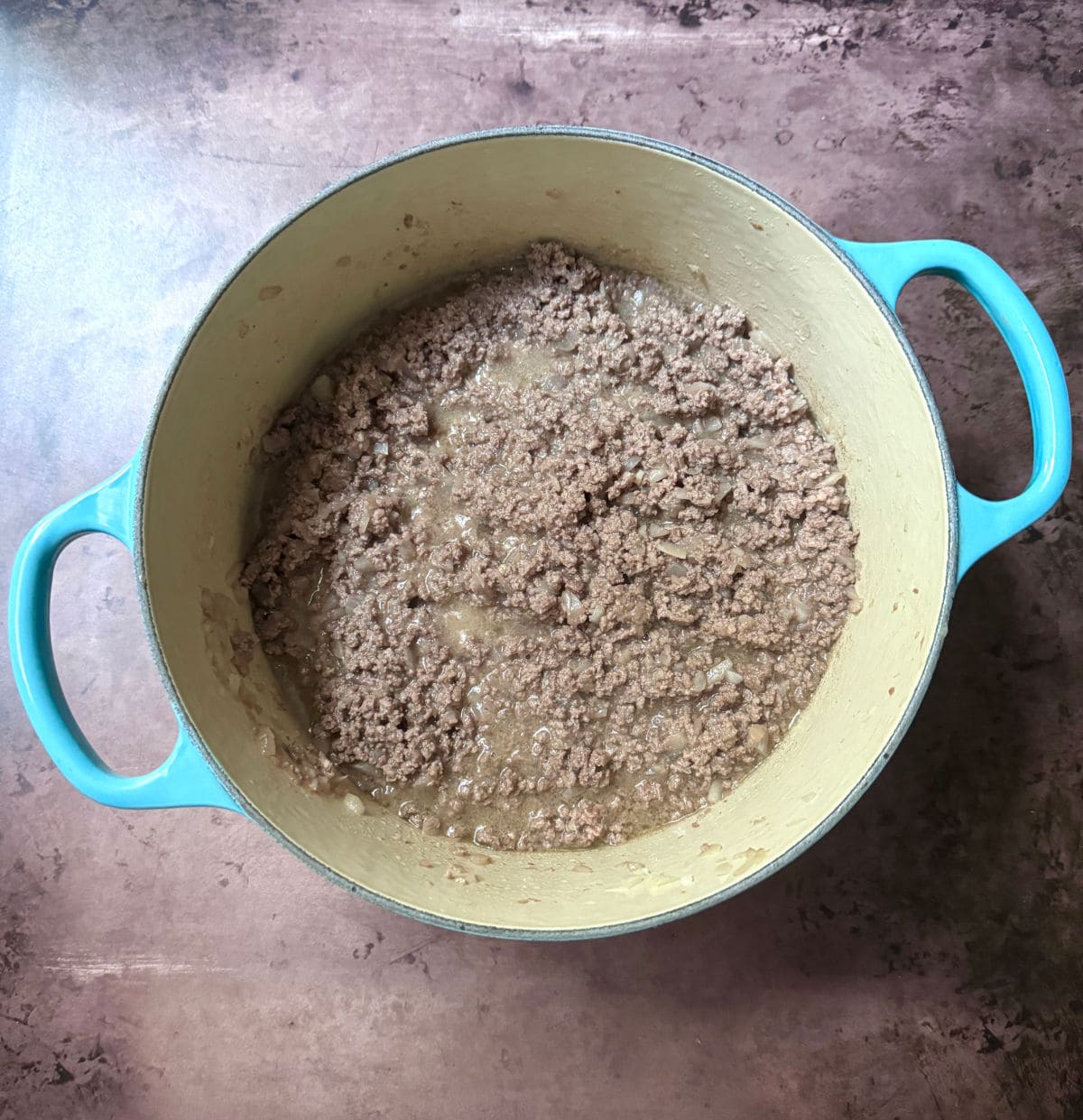 Cooked ground beef in a blue pot on a brown counter.