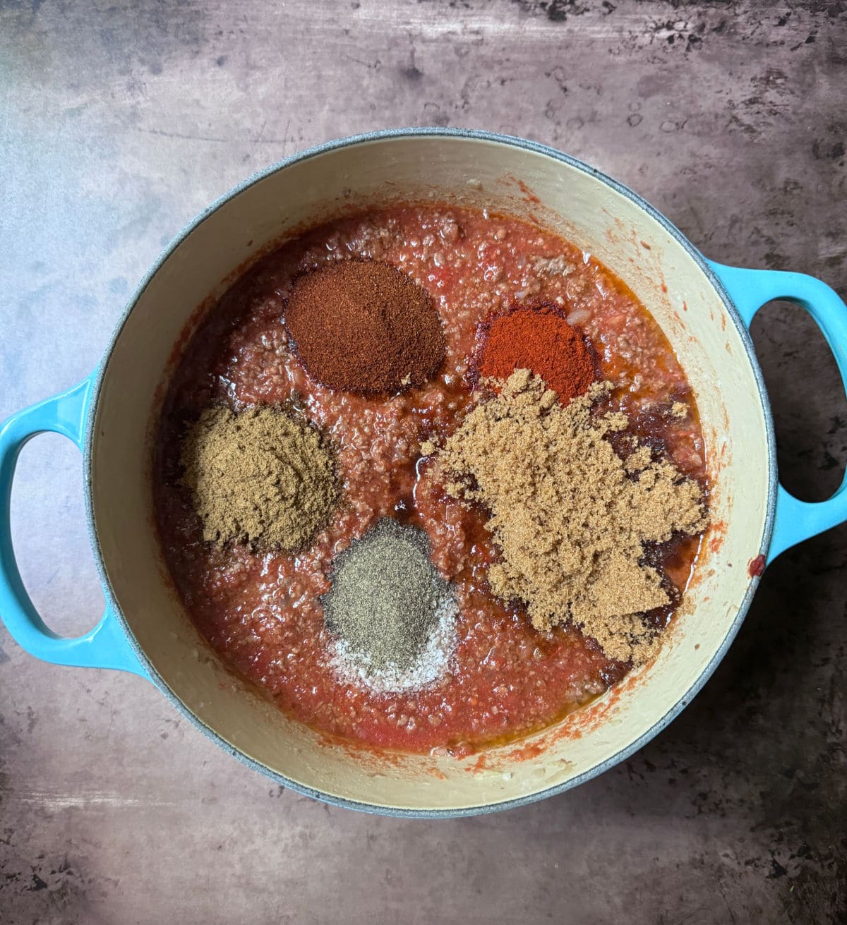 Ground beef with a tomato sauce in a blue pot with spices on top.