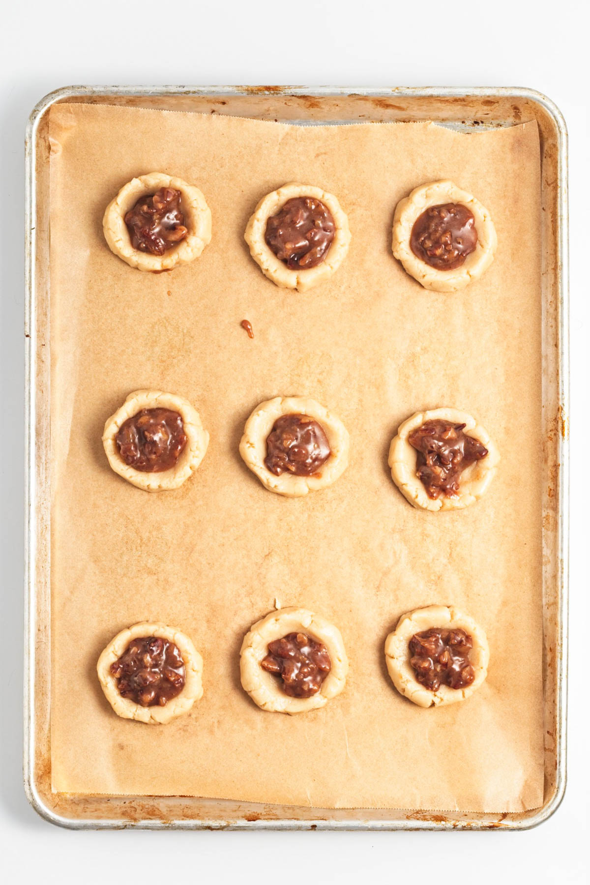 Pecan pie filling in middle of cookies on parchment paper on cookie sheet.