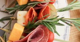 Charcuterie wreath with salami, cheese, rosemary, tomatoes, and pickles on a marble plate.