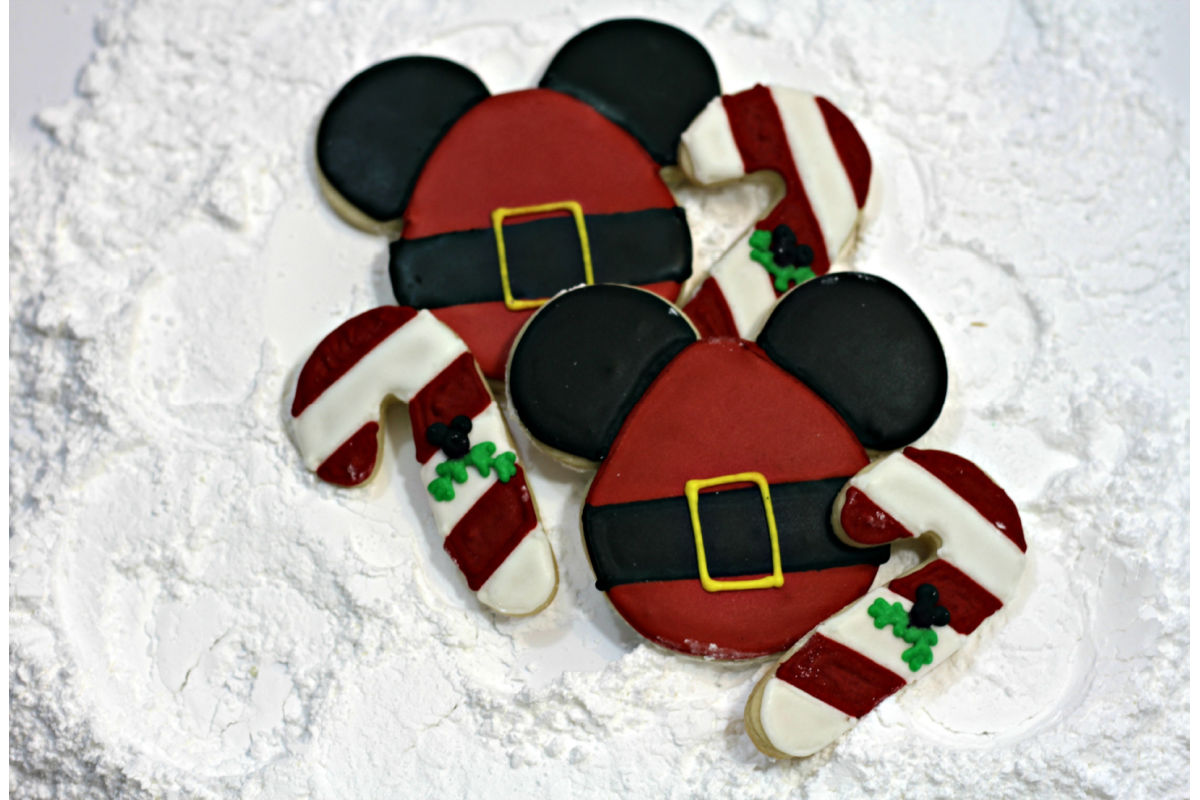 Cookies decorated like Santa Mickey Mouse and candy canes placed on top of powdered sugar.