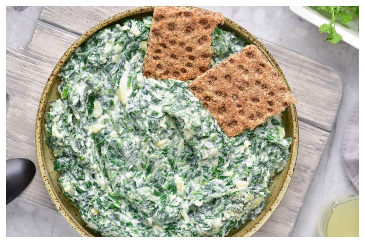 Spinach dip in a brown bowl with two crackers.