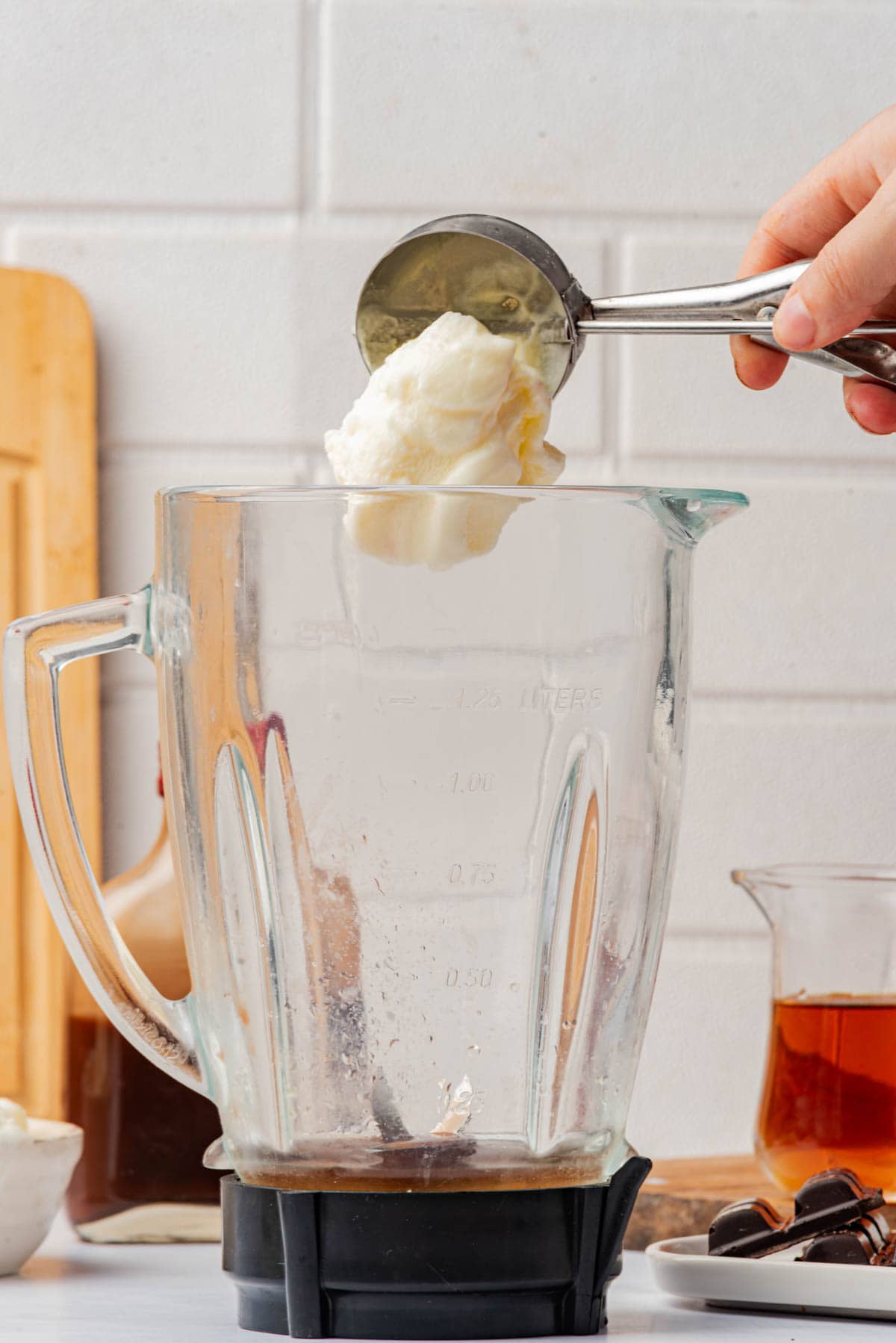 Dropping a scoop of vanilla ice cream into a blender.