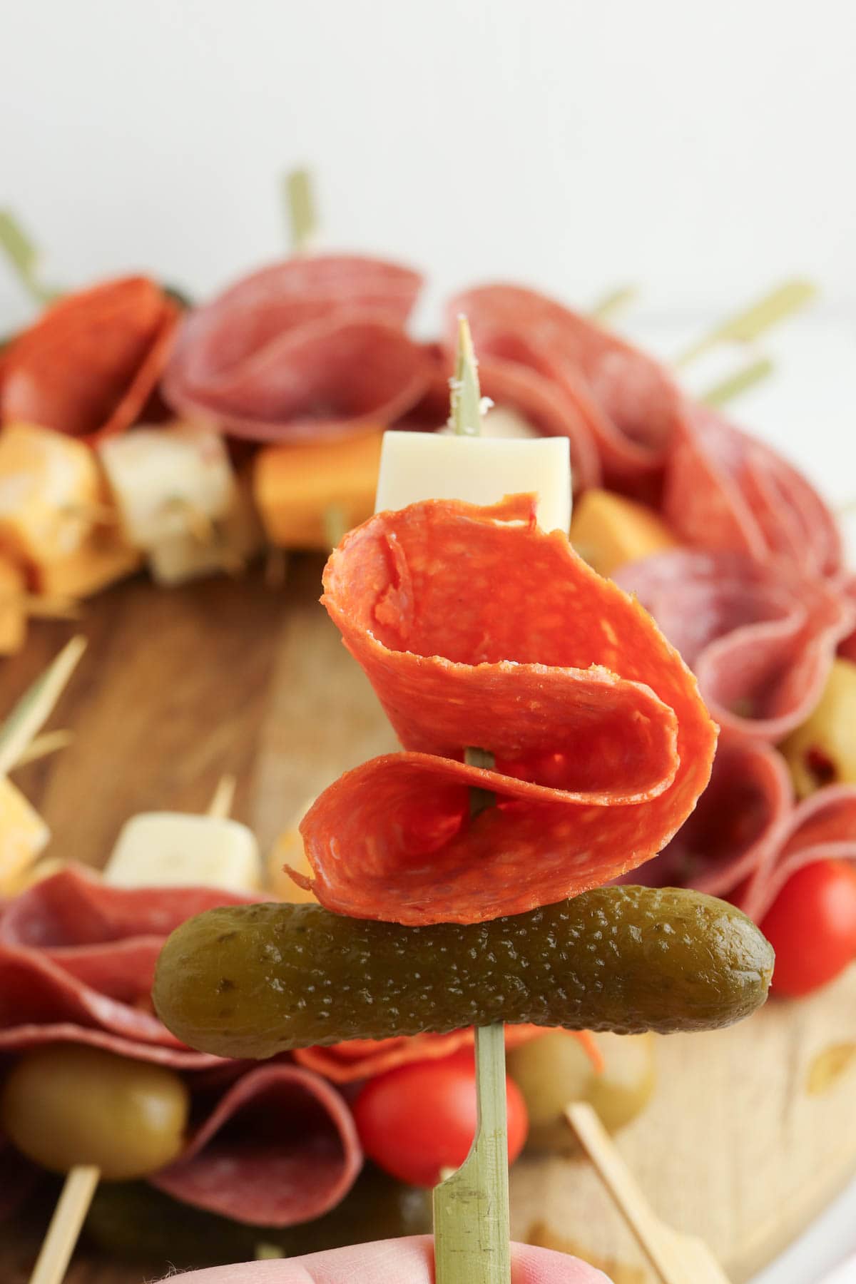 Piece of salami between a cube of cheese and a pickle.