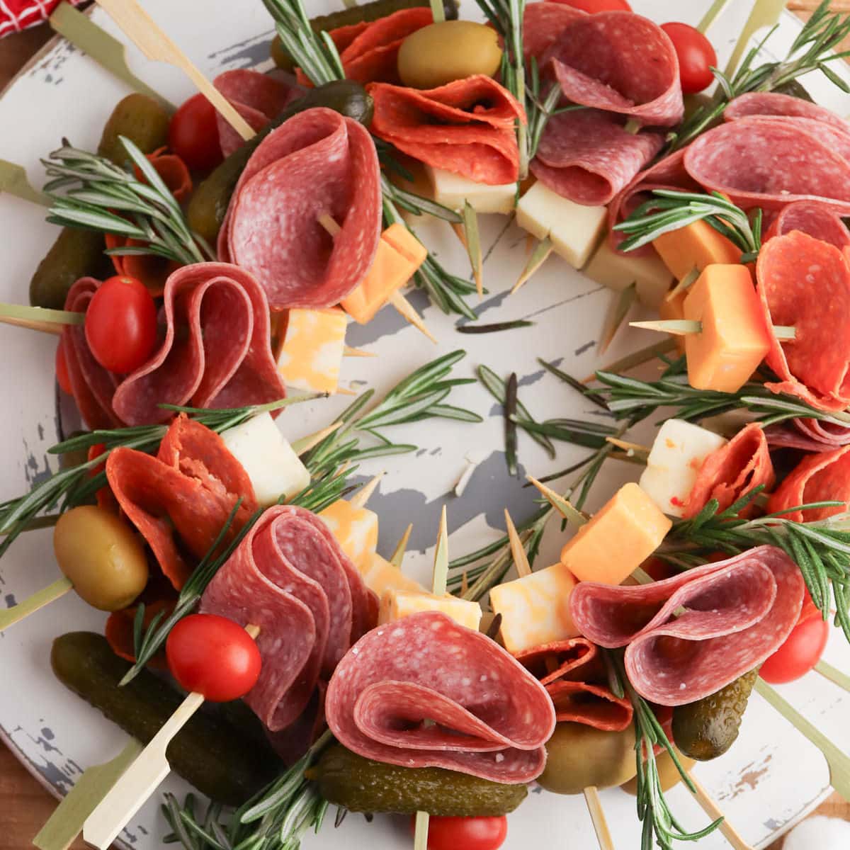 Charcuterie wreath with salami, cheese, rosemary, tomatoes, and pickles on a marble plate.