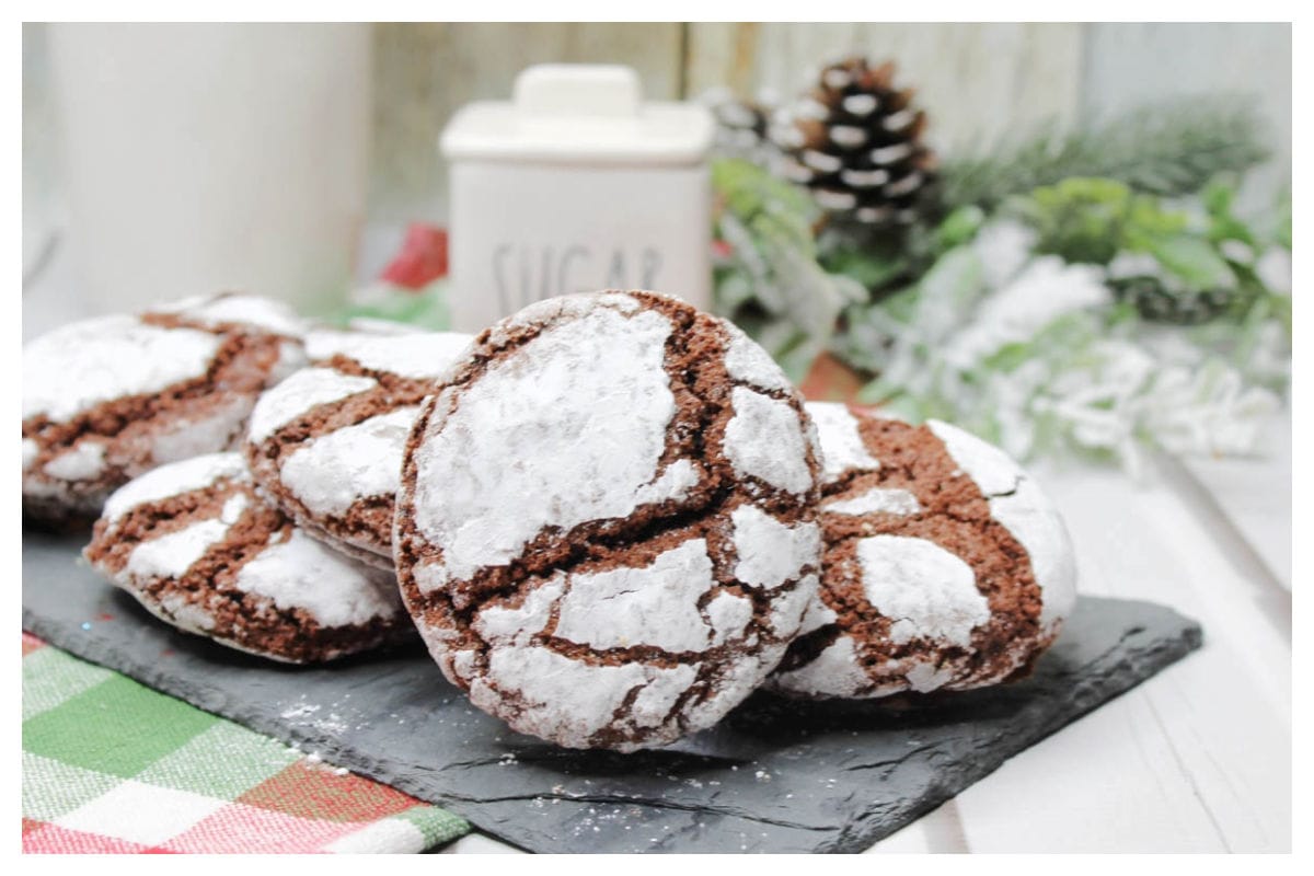 Chocolate crinkle cookies on a black board with holiday decor.