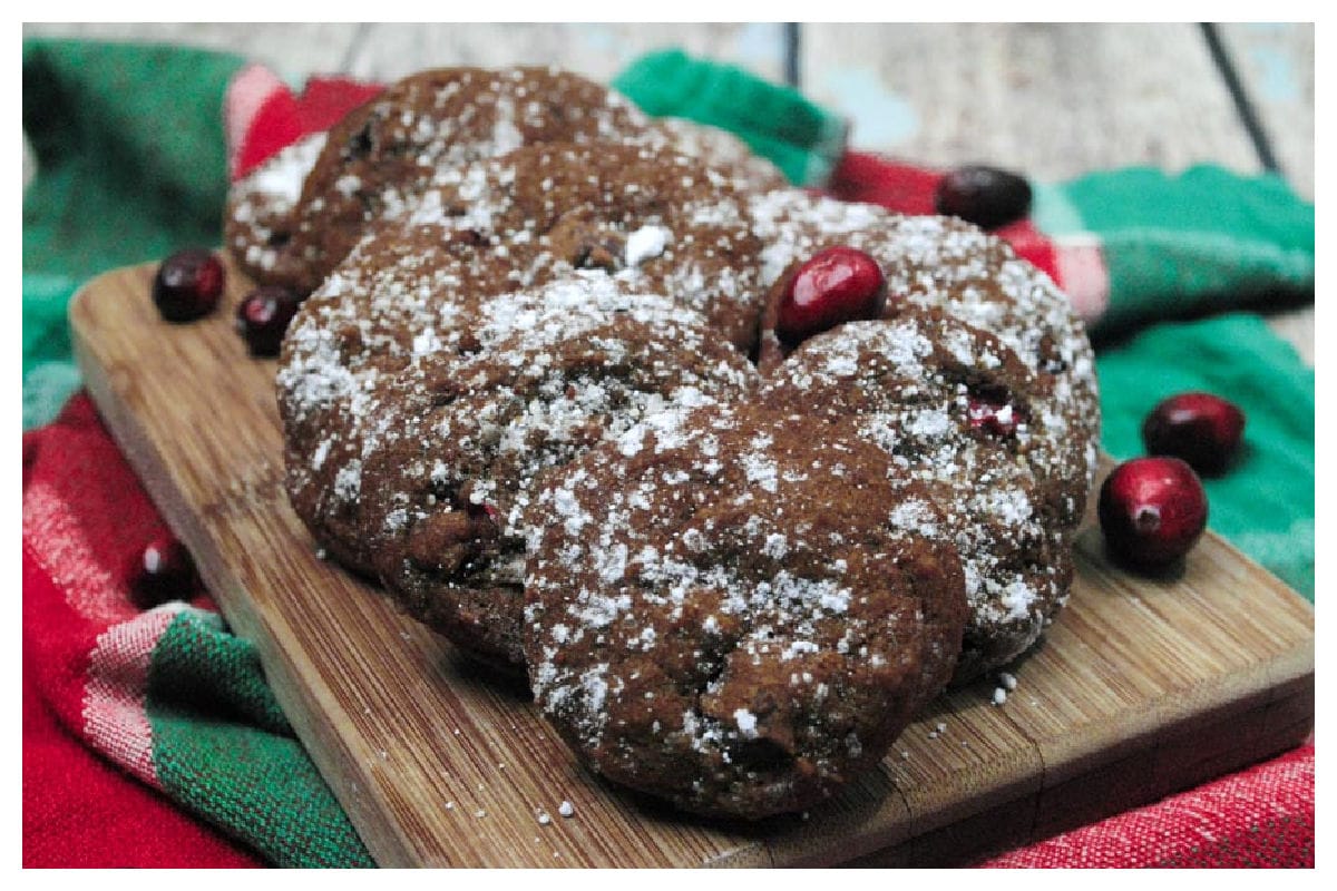 Gingerbread cookies with cranberries on a wood board on red and green cloth with cranberries around.