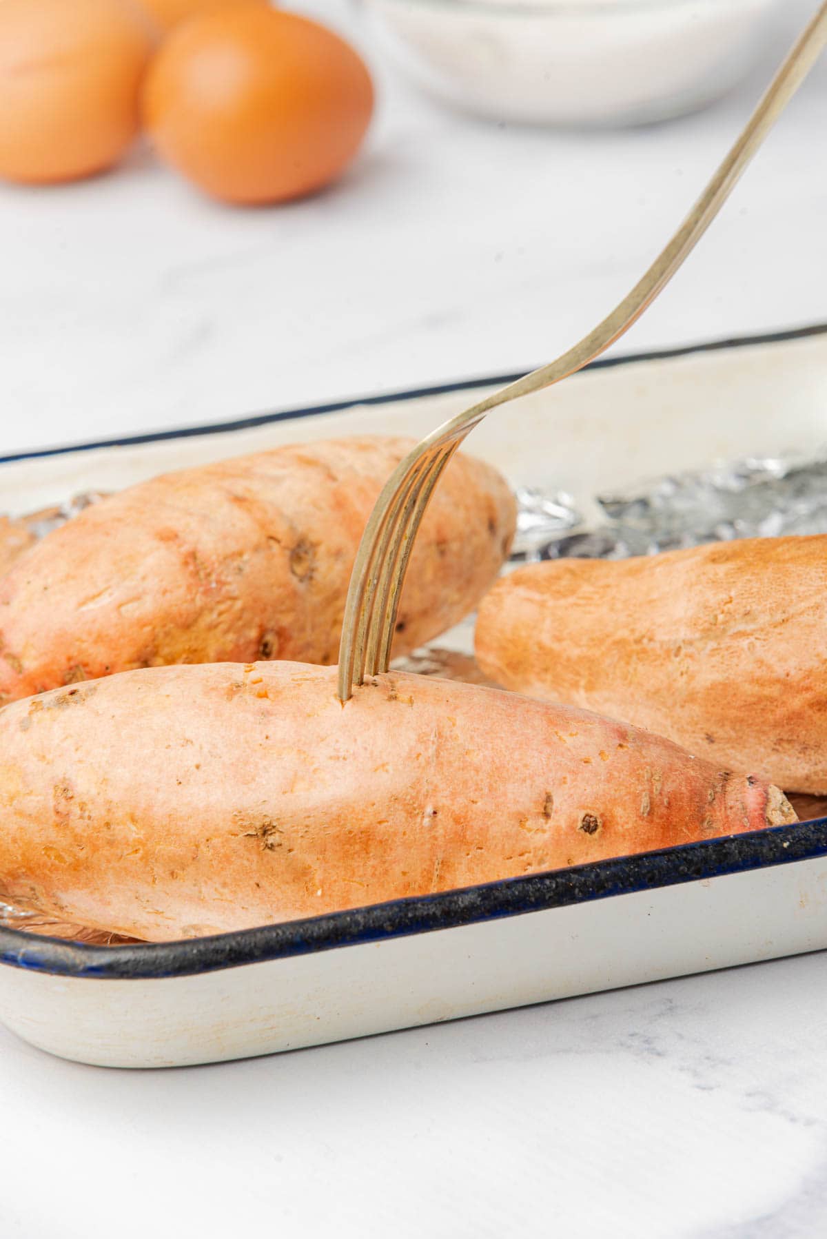 Sweet potatoes in foil lined baking dish with eggs in background.