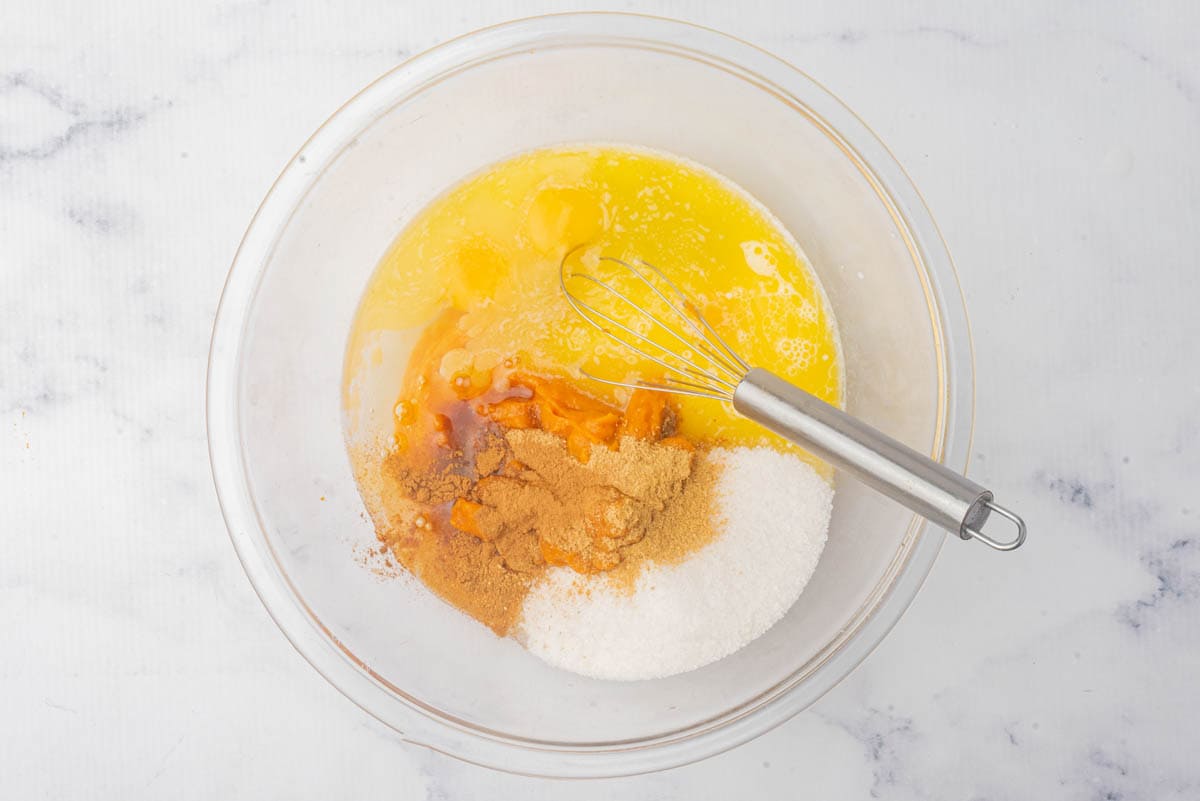 Sweet potatoes with butter, sugar, brown sugar, and eggs in a glass measuring bowl.