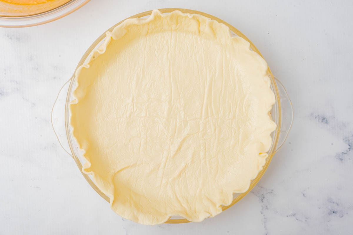 Premade pie shell in a glass pie pan on a marble counter.