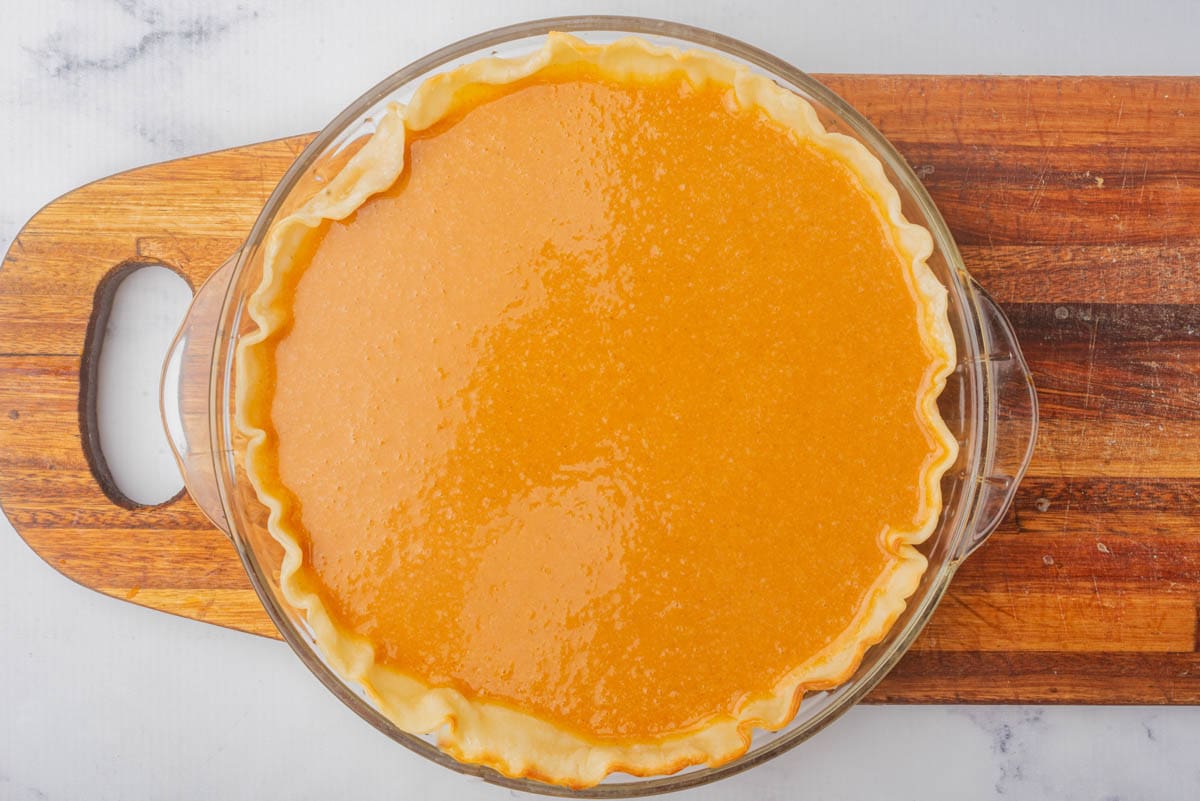 Sweet potato pie in a glass pie dish on a wood cutting board.