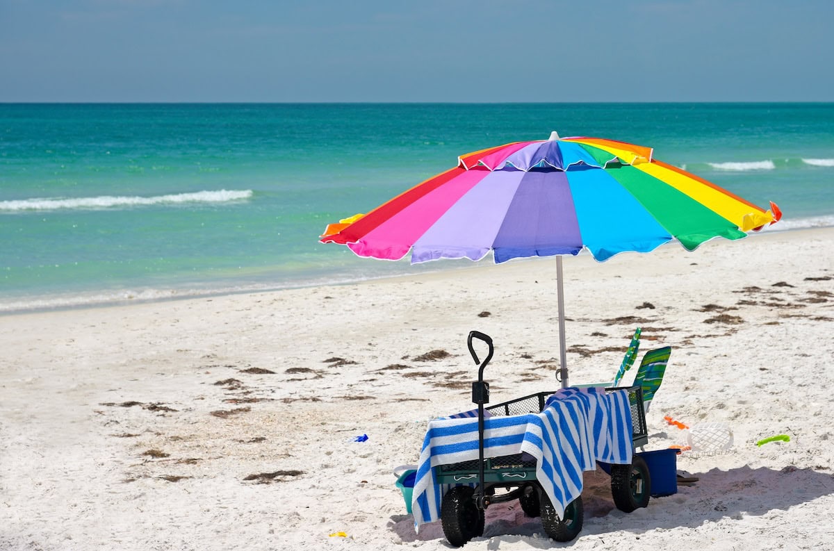 Colorful Beach Umbrella with a Wagon, Striped Towel, Chair and Toys on the Beach