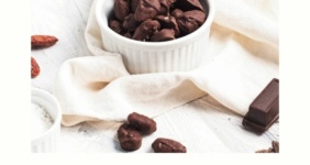 Chocolate covered almonds in a bowl on a shite napkin with a jar of more behind and a small bowl of raw almonds in background.