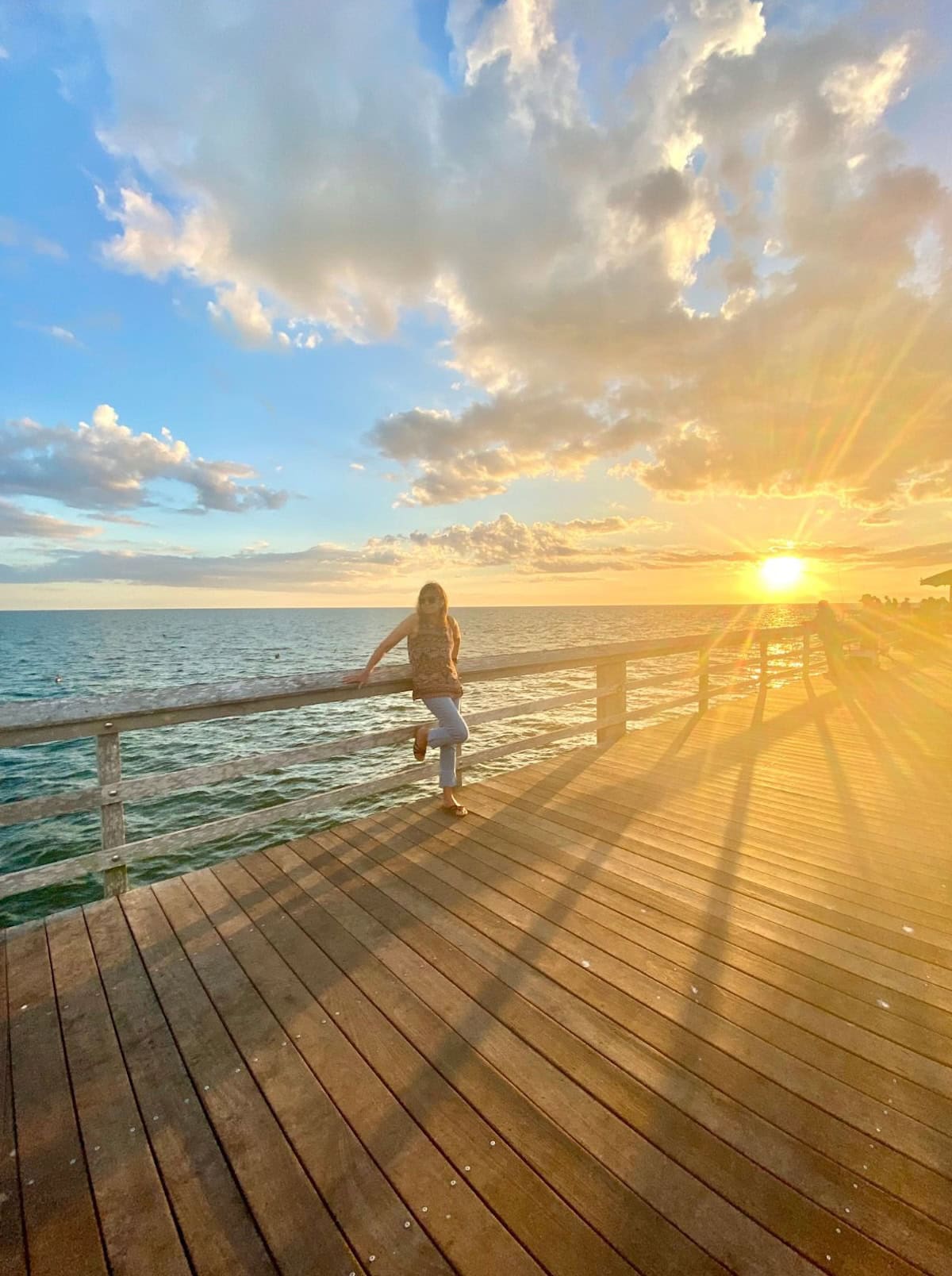 Woman leaning on side of pier at sunset.