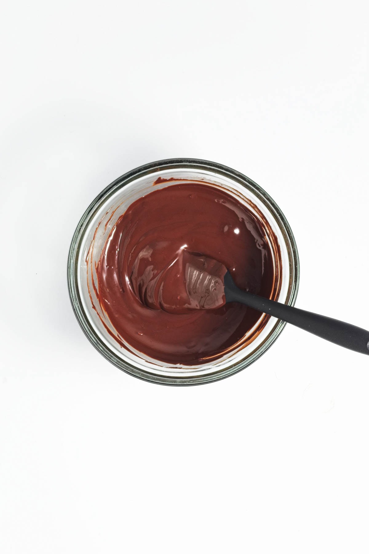 Melted chocolate in a glass bowl with a spatula.