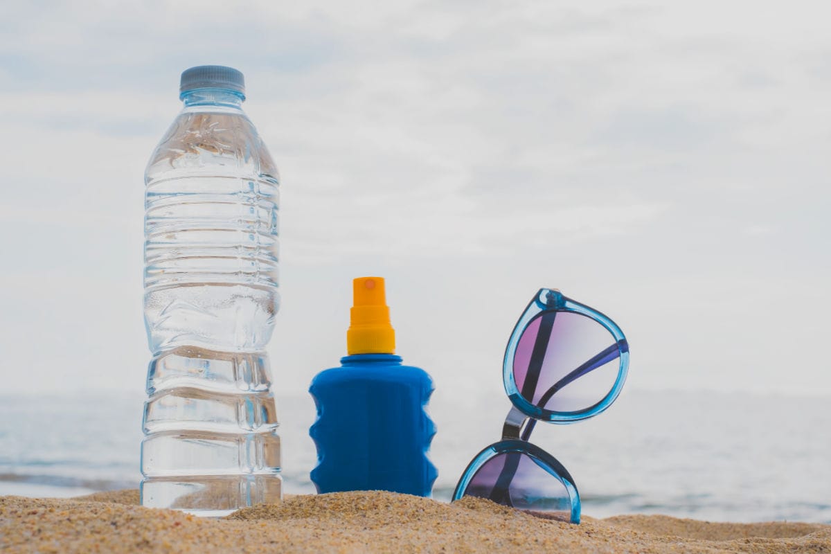 Botlle of water, sunscreen, and sunglasses in sand.