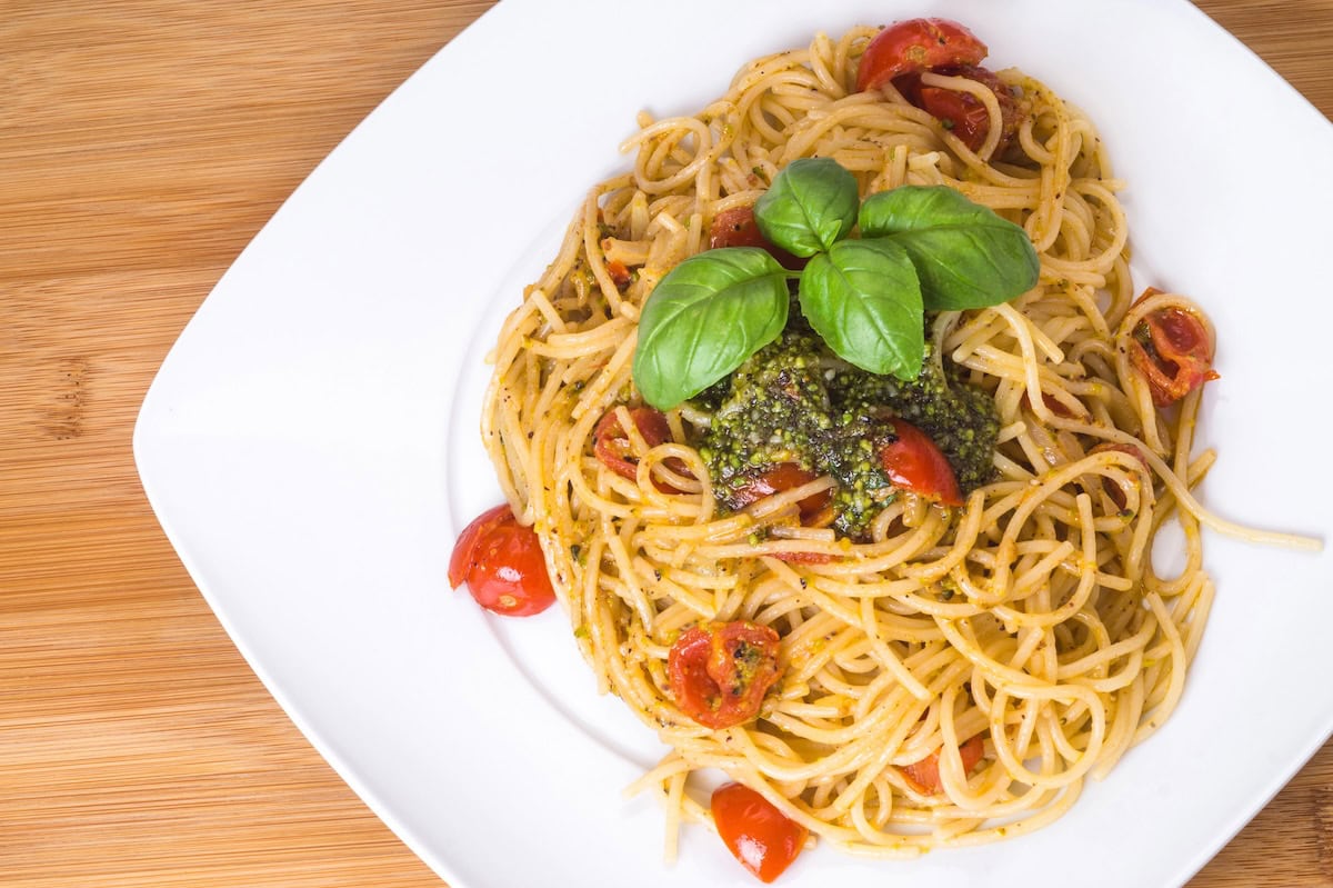 Apaghetti with cherry tomatoes and pistachio pesto on a white plate.