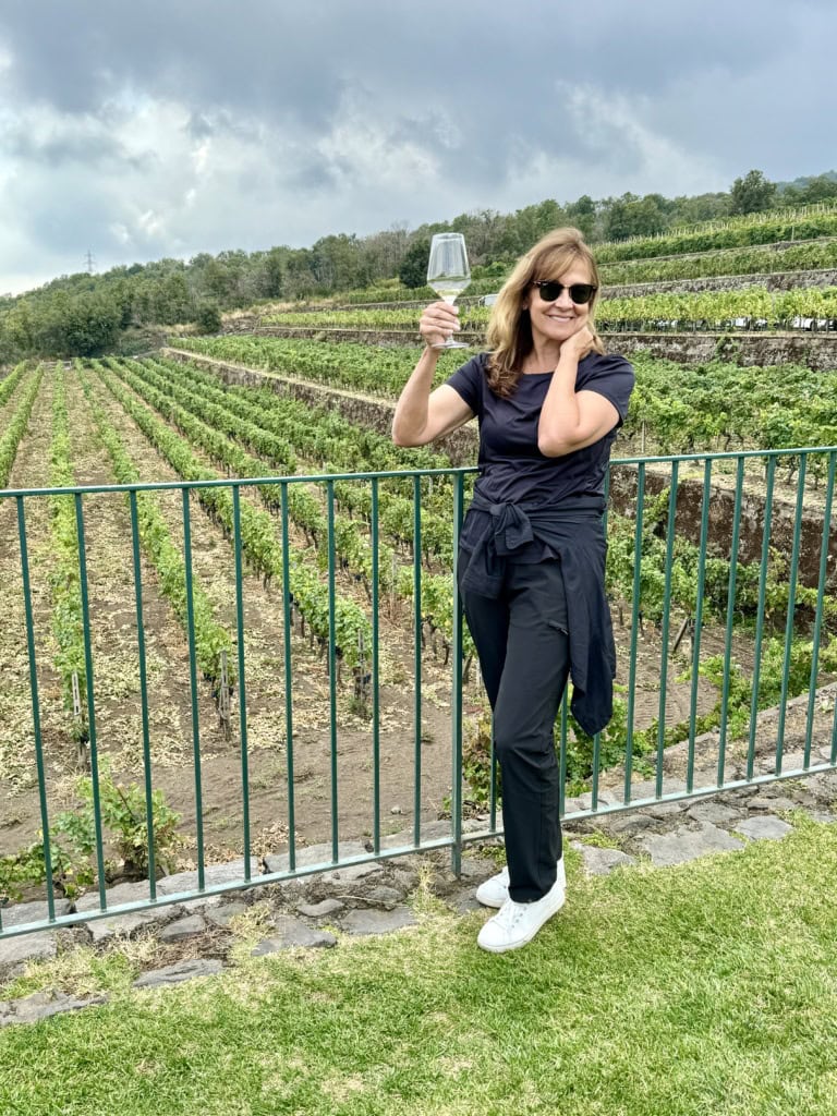 Woman holding up a glass of wine in front of a vineyard.