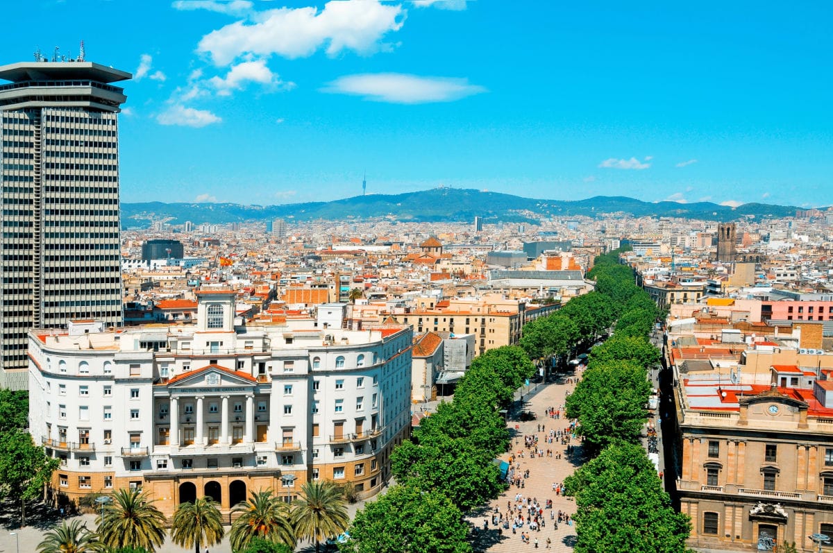 View of a busy street in a city with mountains and blue sky.