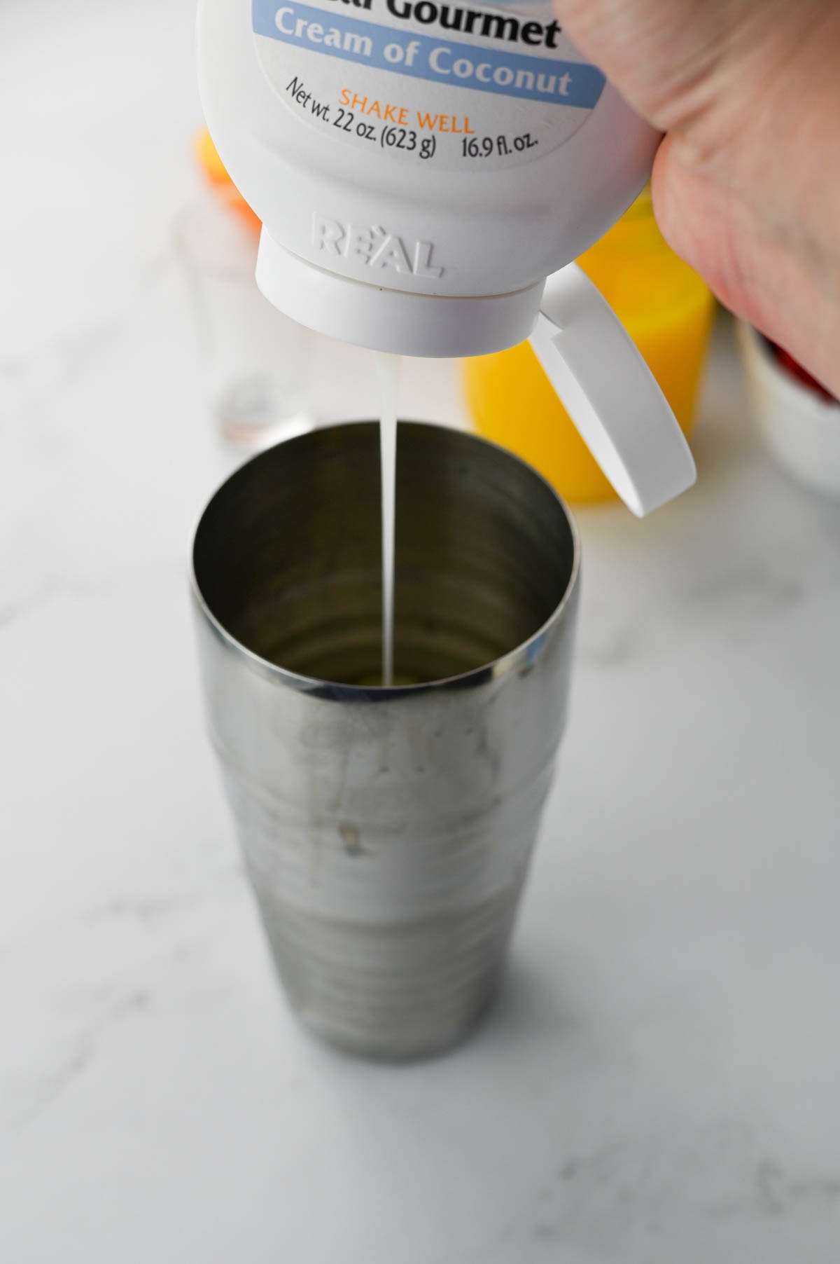 Pouring cream of coconut into a cocktail shaker.