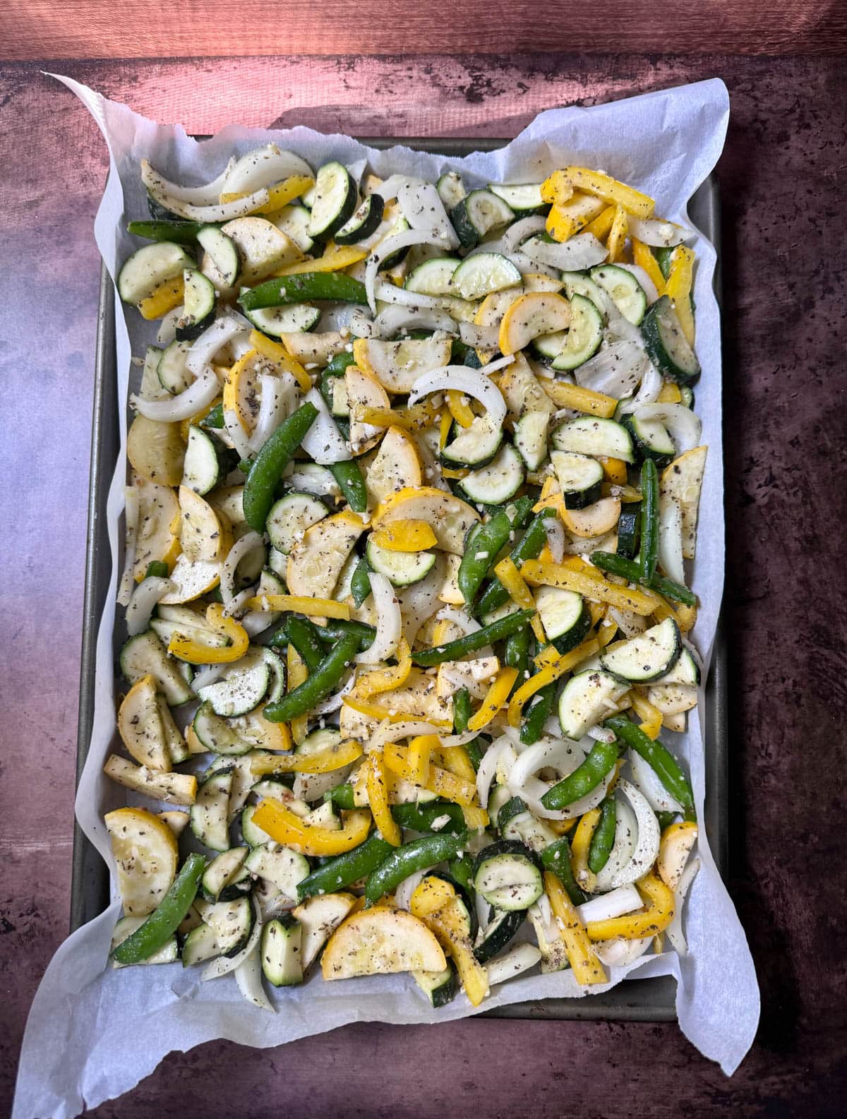 Uncooked vegetables with seasoning on a baking tray lined with parchment paper.