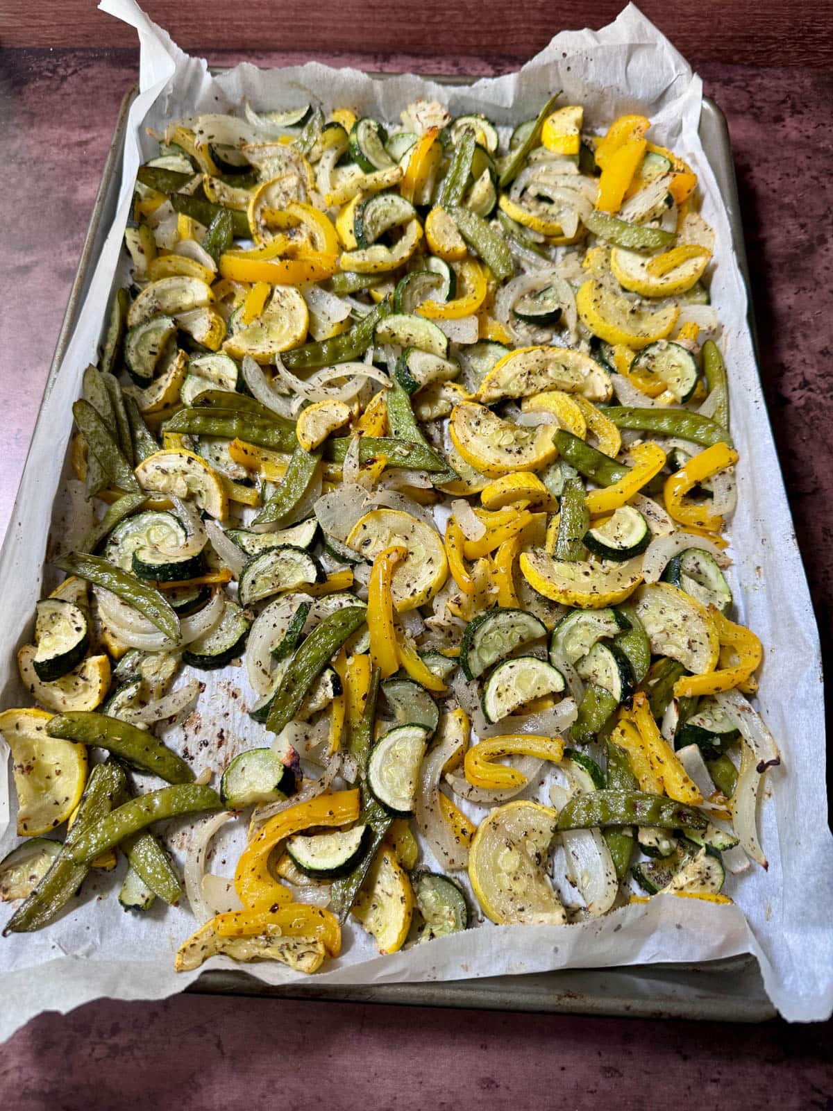 Cooked vegetables with seasoning on a baking tray lined with parchment paper.