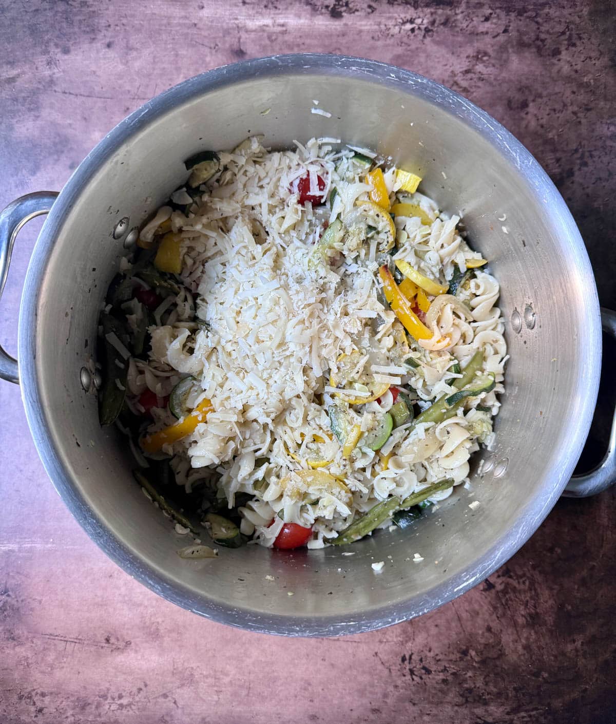 Parmesan cheese on top of vegetables and pasta in a large pot.