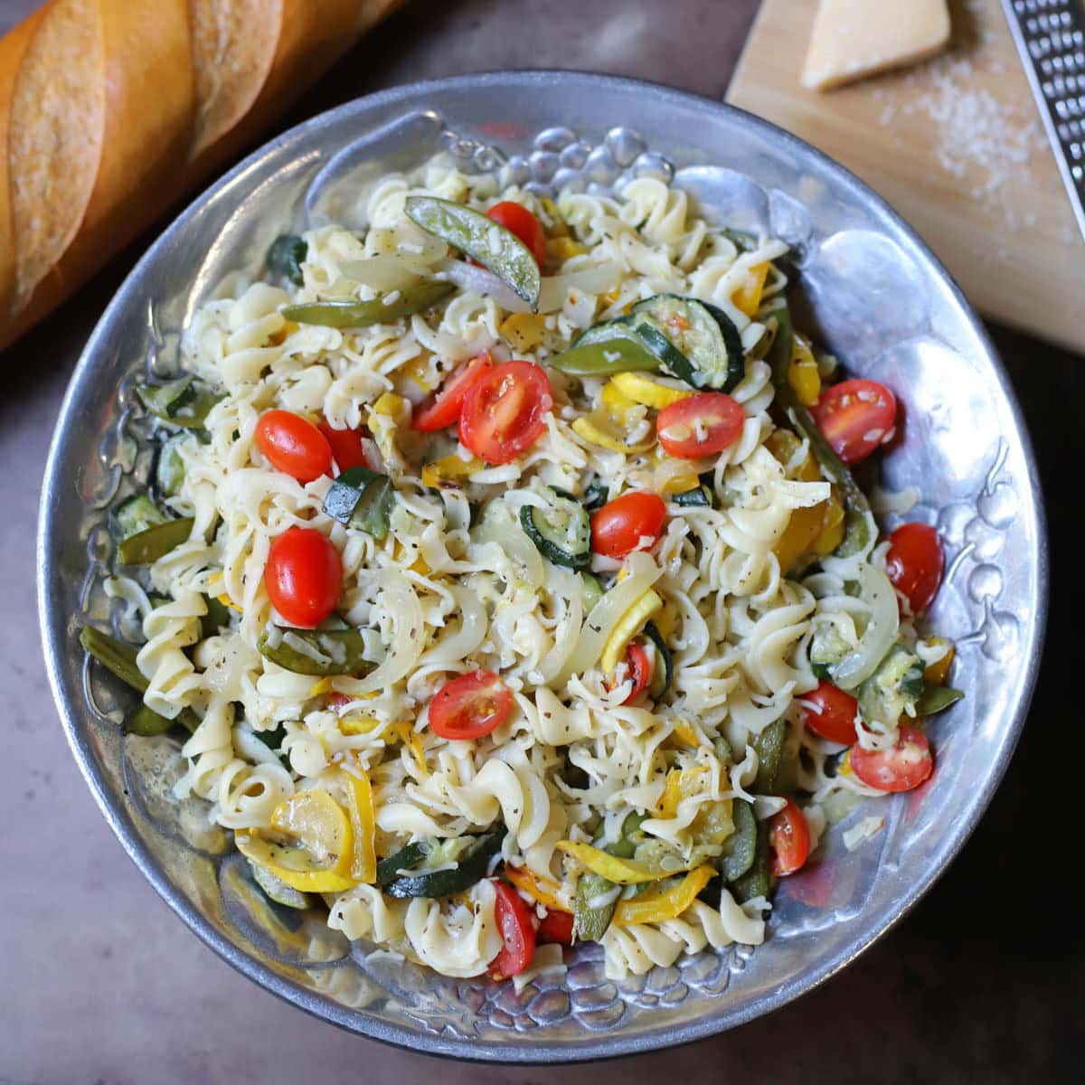 Pasta and roasted vegetables with parmesan cheese in a silver bowl.