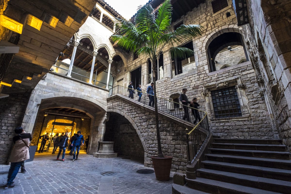 Stone building with bridge walkway and people walking around.