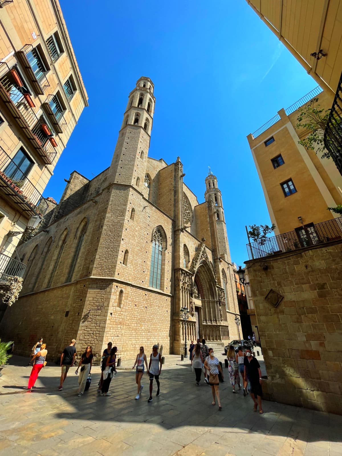 Stone church with tall columns against a blue sky with people walking around.