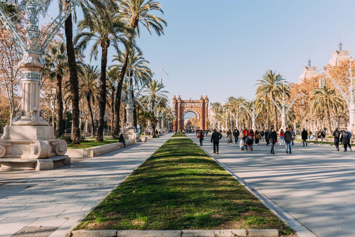 An archway with people walking on walkway with palm tress and a blue sky.