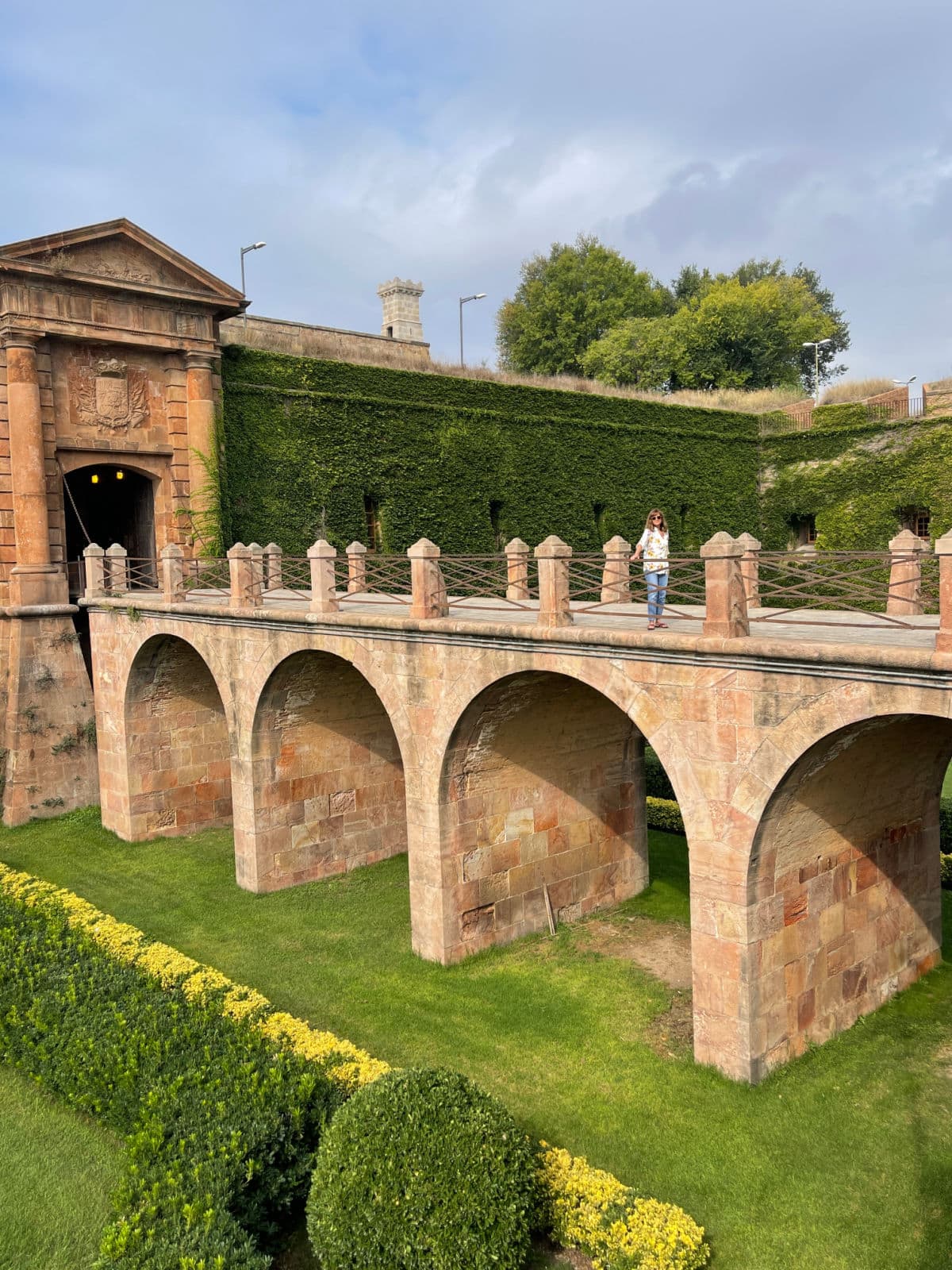 Old Fort with bridge over green grass with woman standing on bridge.