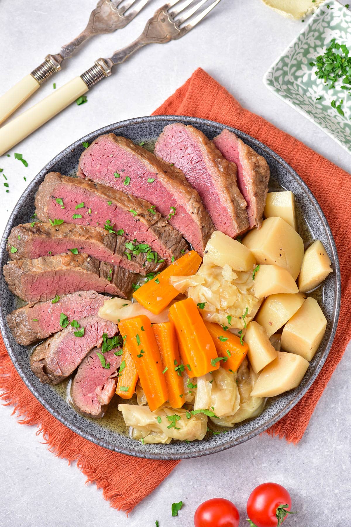 Sliced corned beef, carrots, cabbage, and potatoes on a grey plate over an orange napkin.