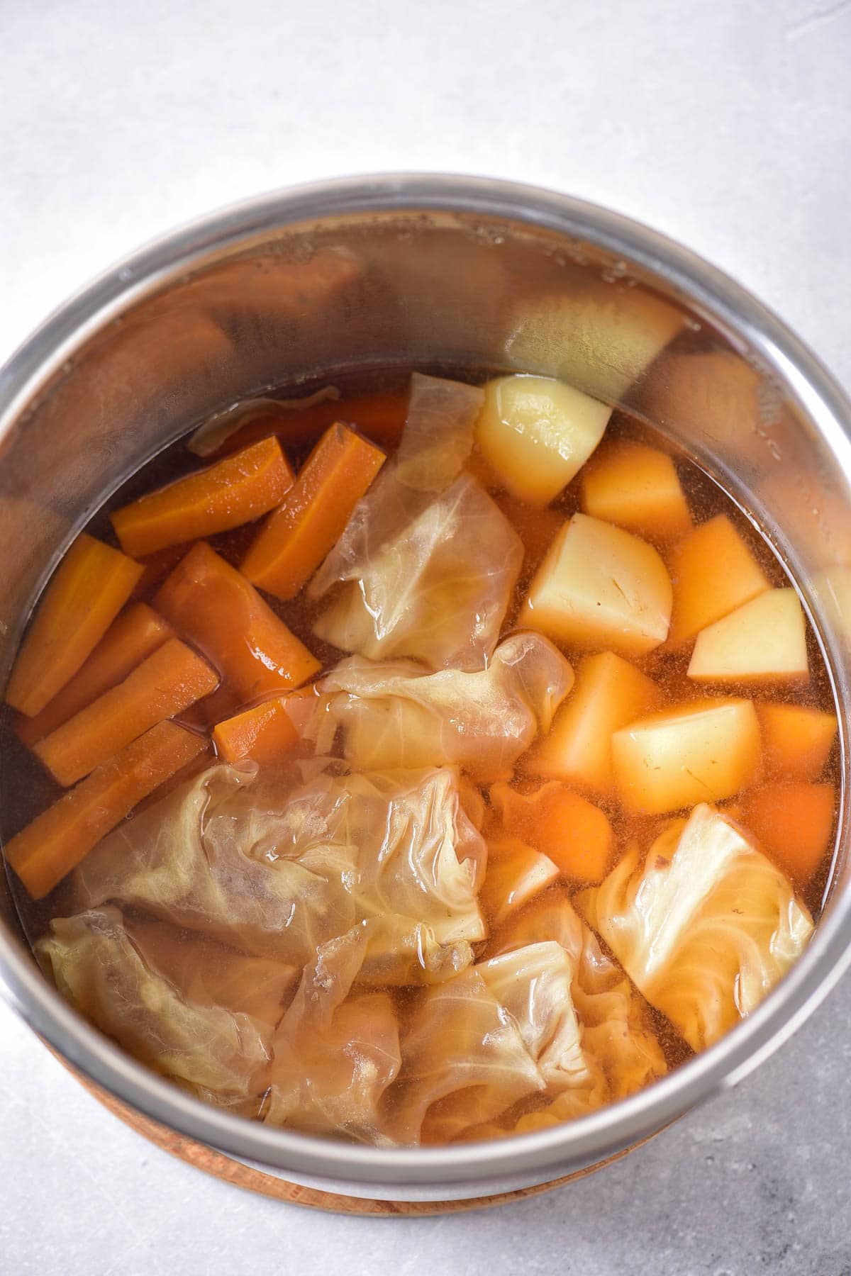 Sliced carrots, cubed potatoes, and cubed cabbage in broth in a white bowl on a grey background.