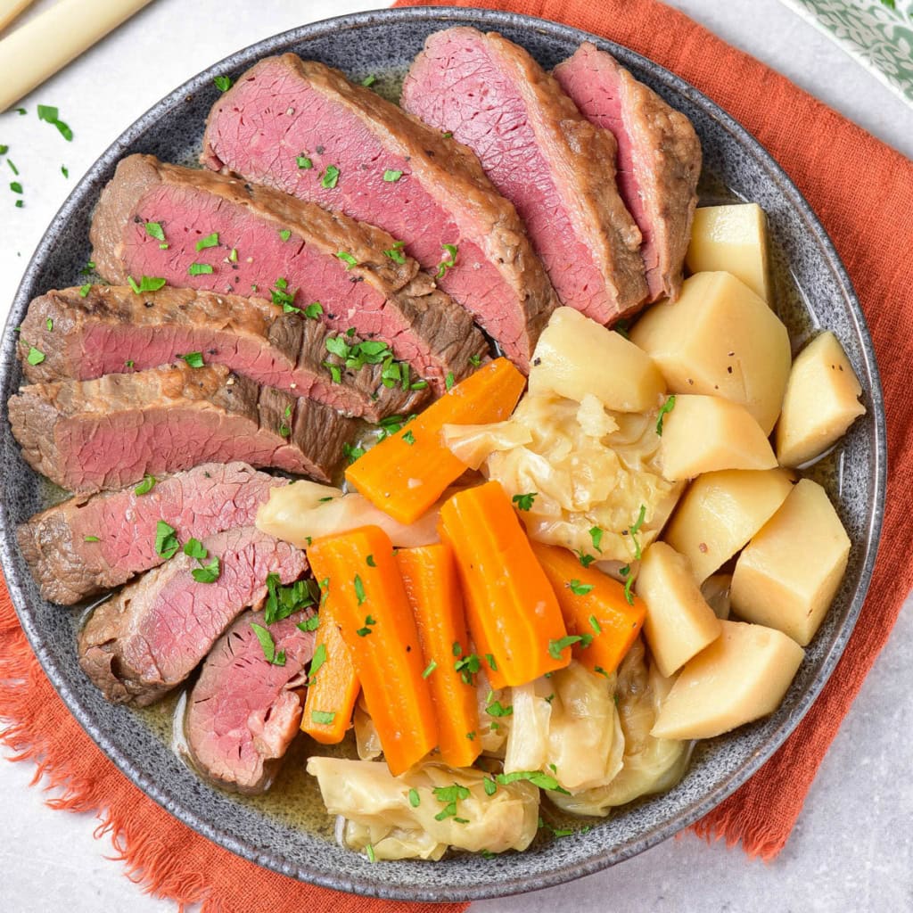 Sliced corned beef, carrots, cabbage, and potatoes on a grey plate over an orange napkin.