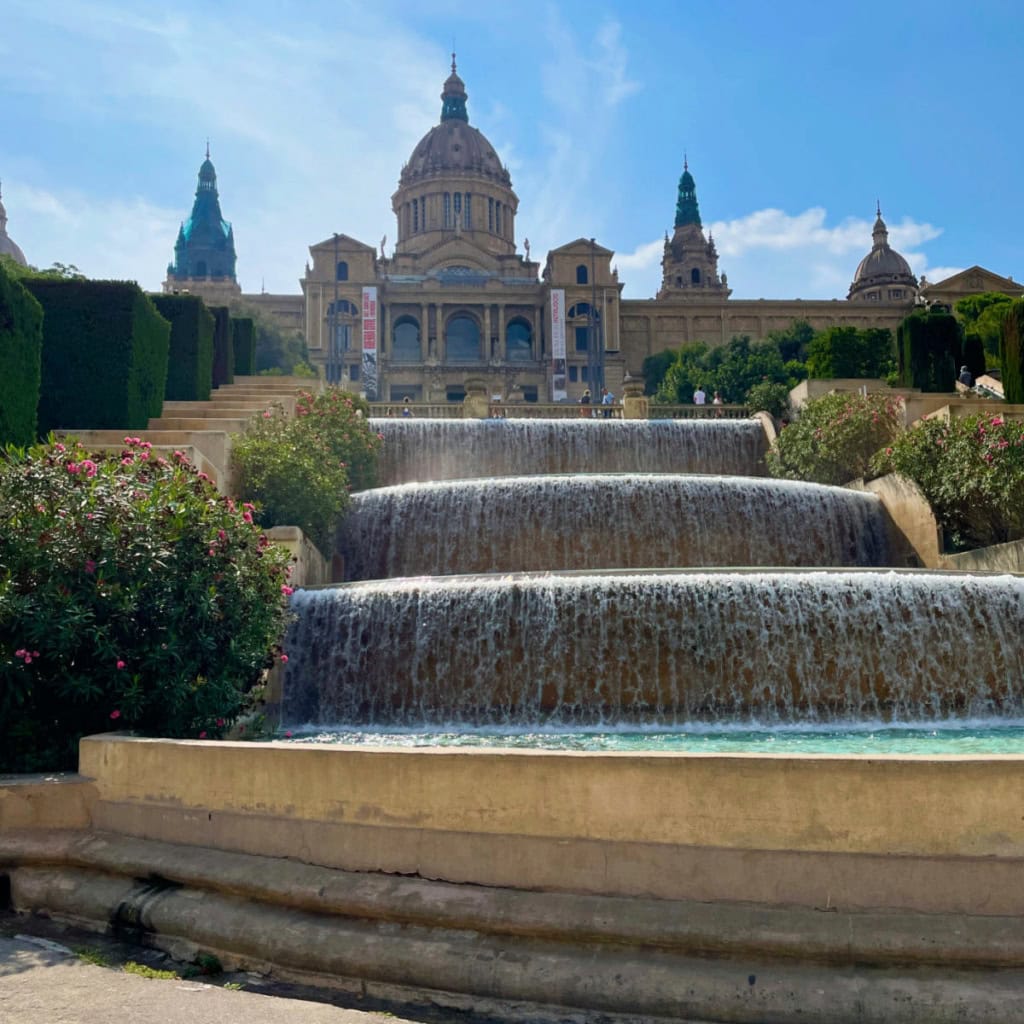 Huge water fountains in front of historic building against a blue sky.