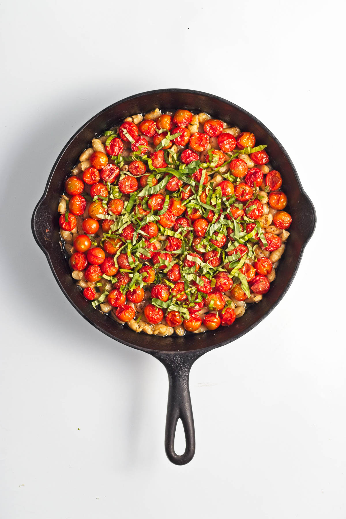 Baked tomatoes with beans, garlic, and oil in a cast iron skillet, topped with herbs.