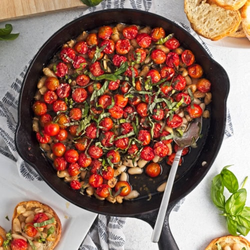 Baked tomatoes with beans, garlic, and oil in a cast iron skillet, topped with herbs.