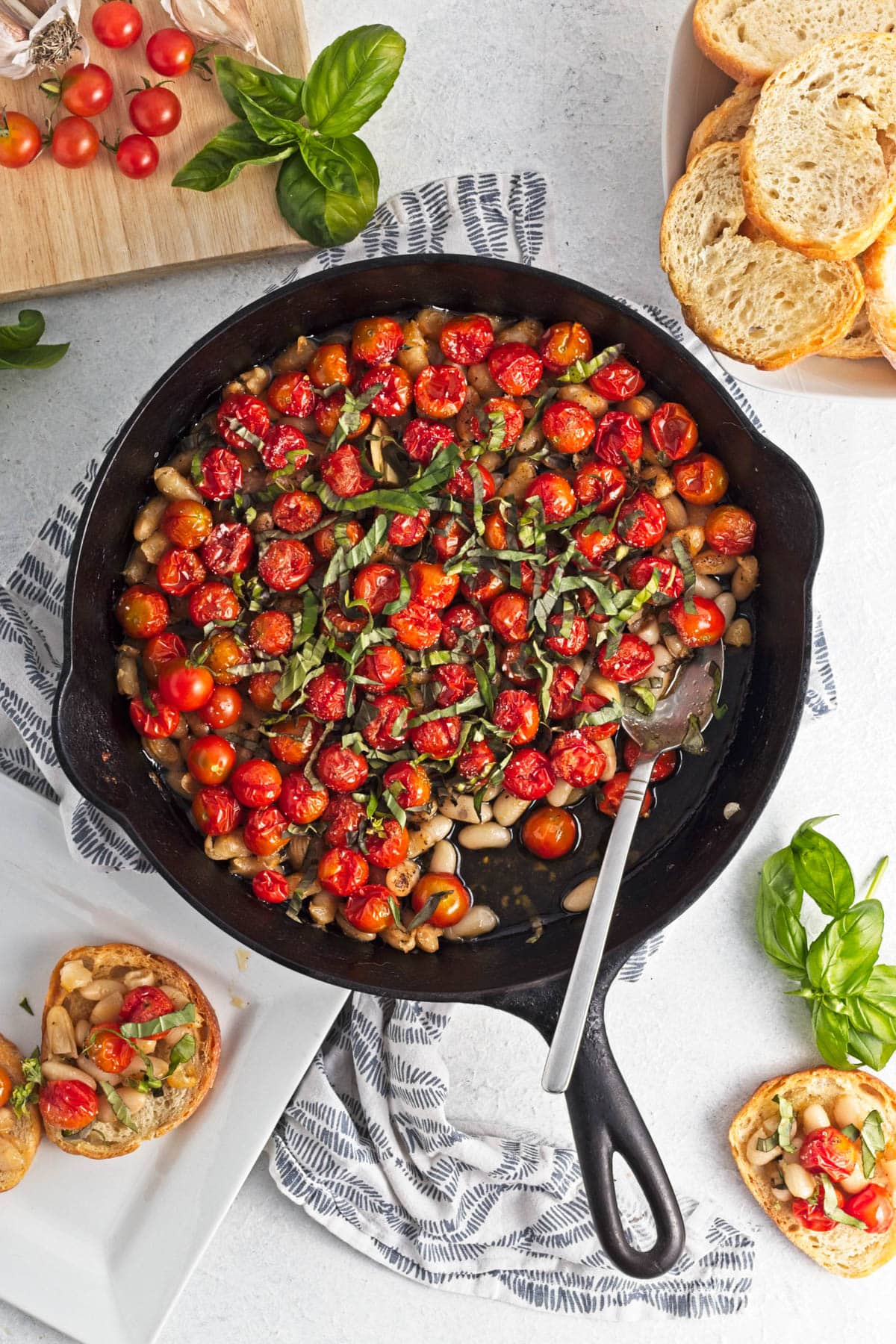 Baked tomatoes with beans, garlic, and oil in a cast iron skillet, topped with herbs.