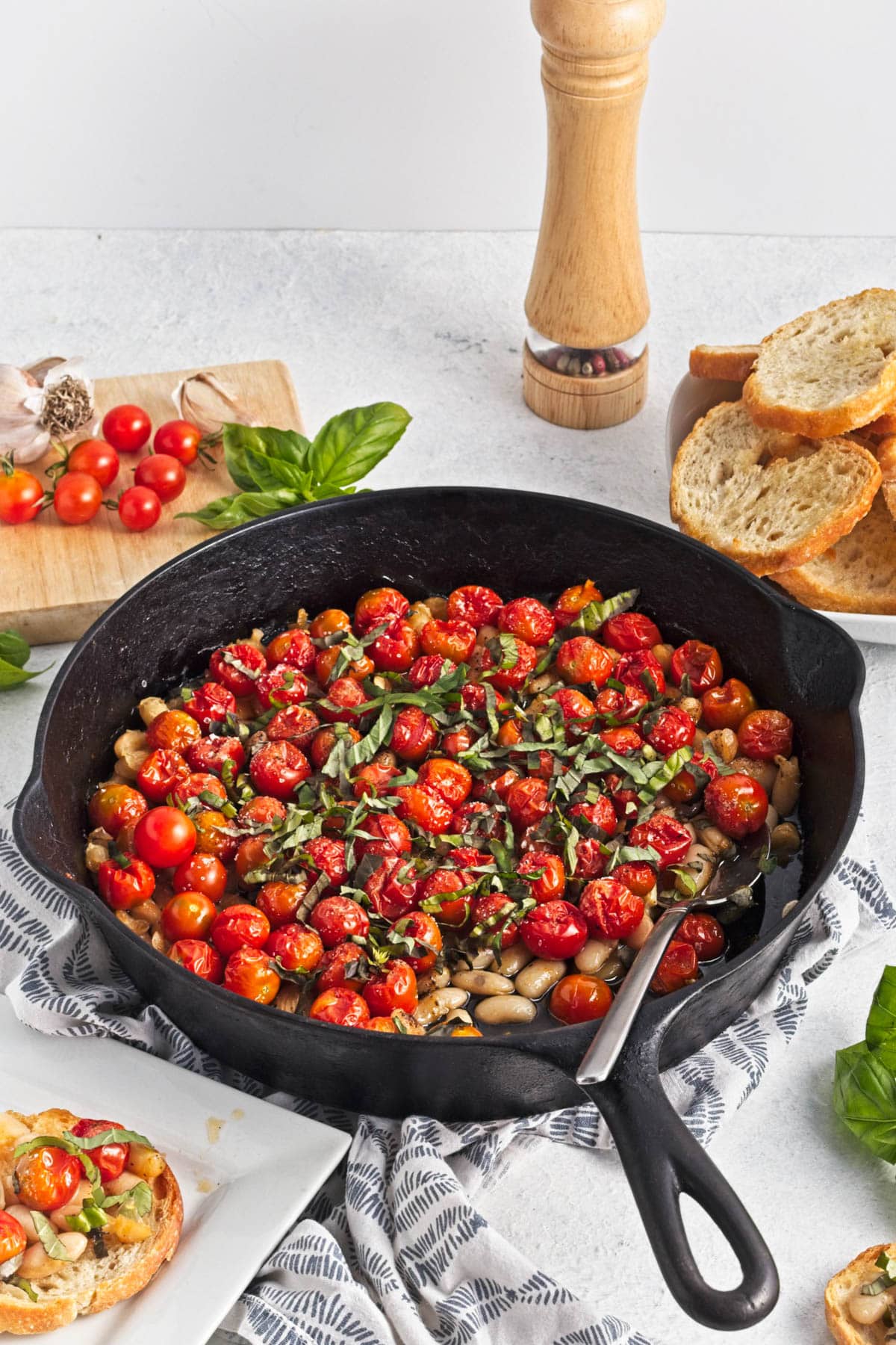 Baked tomatoes with beans, garlic, and oil in a cast iron skillet, topped with herbs.