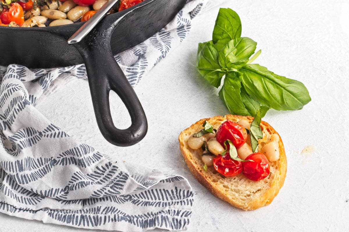 Tomato crostini with basil  on marble counter with pan in background.