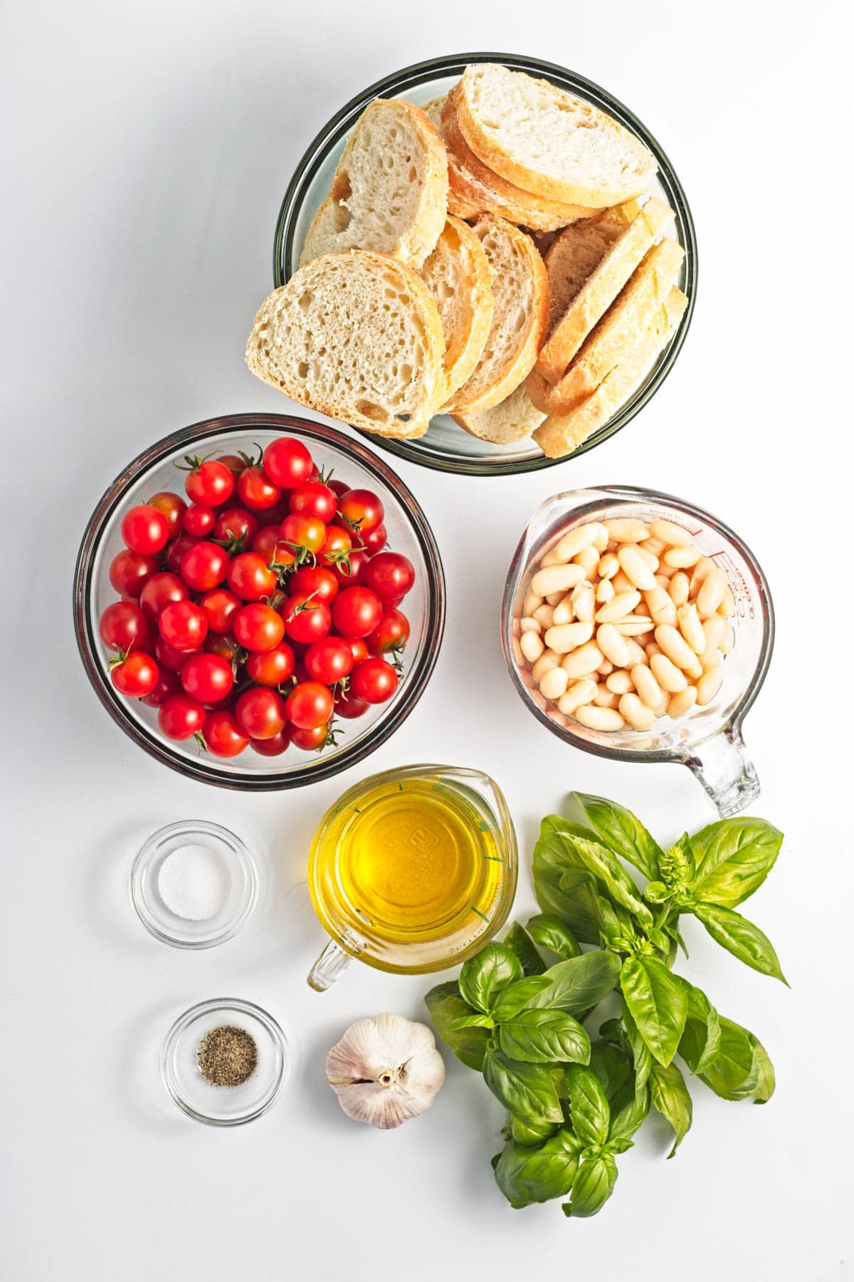 Glass bowls of bread, tomatoes, garlic, beans, salt, pepper, and olive oil