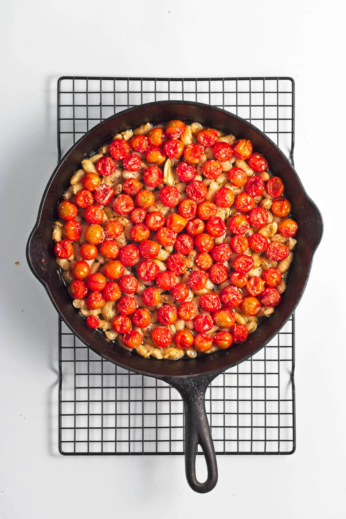 Baked tomatoes with beans, garlic, and oil in a cast iron skillet.