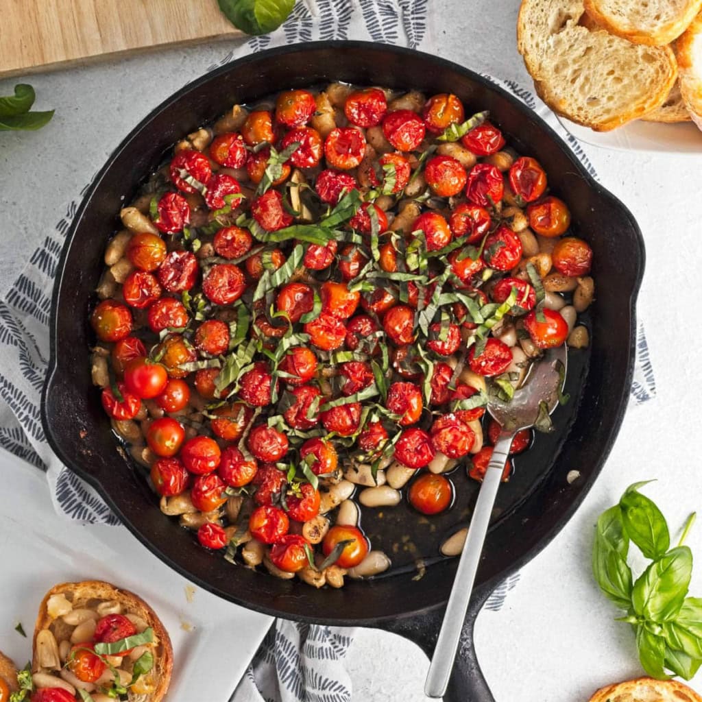 Baked tomatoes with beans, garlic, and oil in a cast iron skillet.