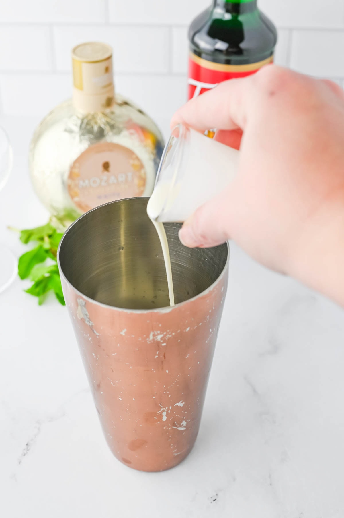 Pouring white cream liquid into a copper shaker.