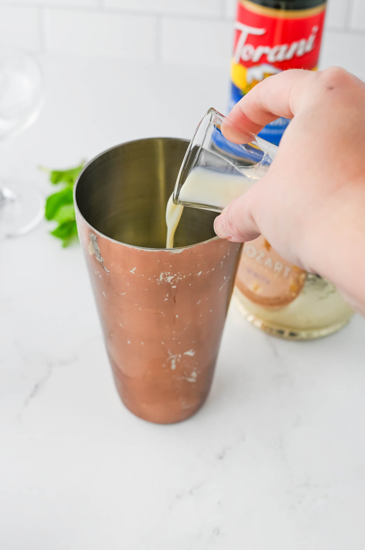 Pouring cream colored liquid into a copper shaker.