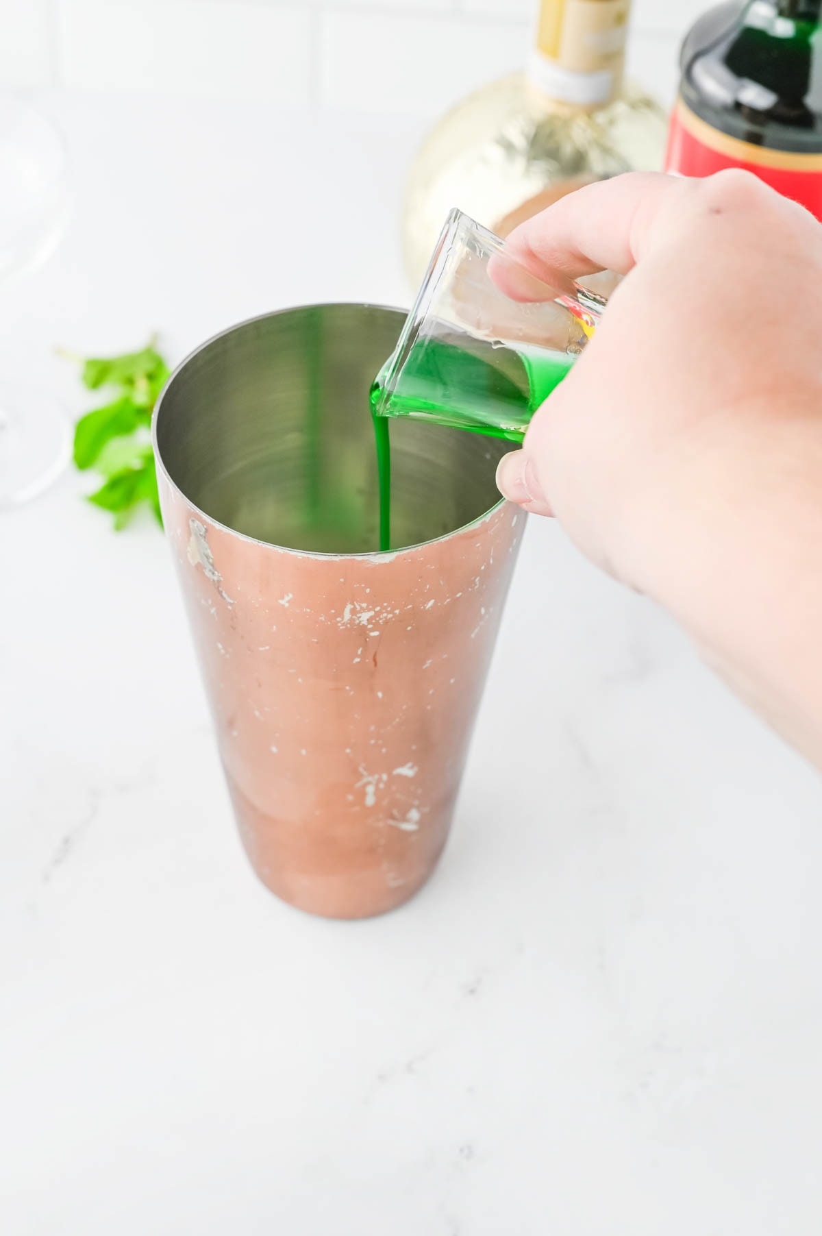 Pouring green liquid into a copper shaker.