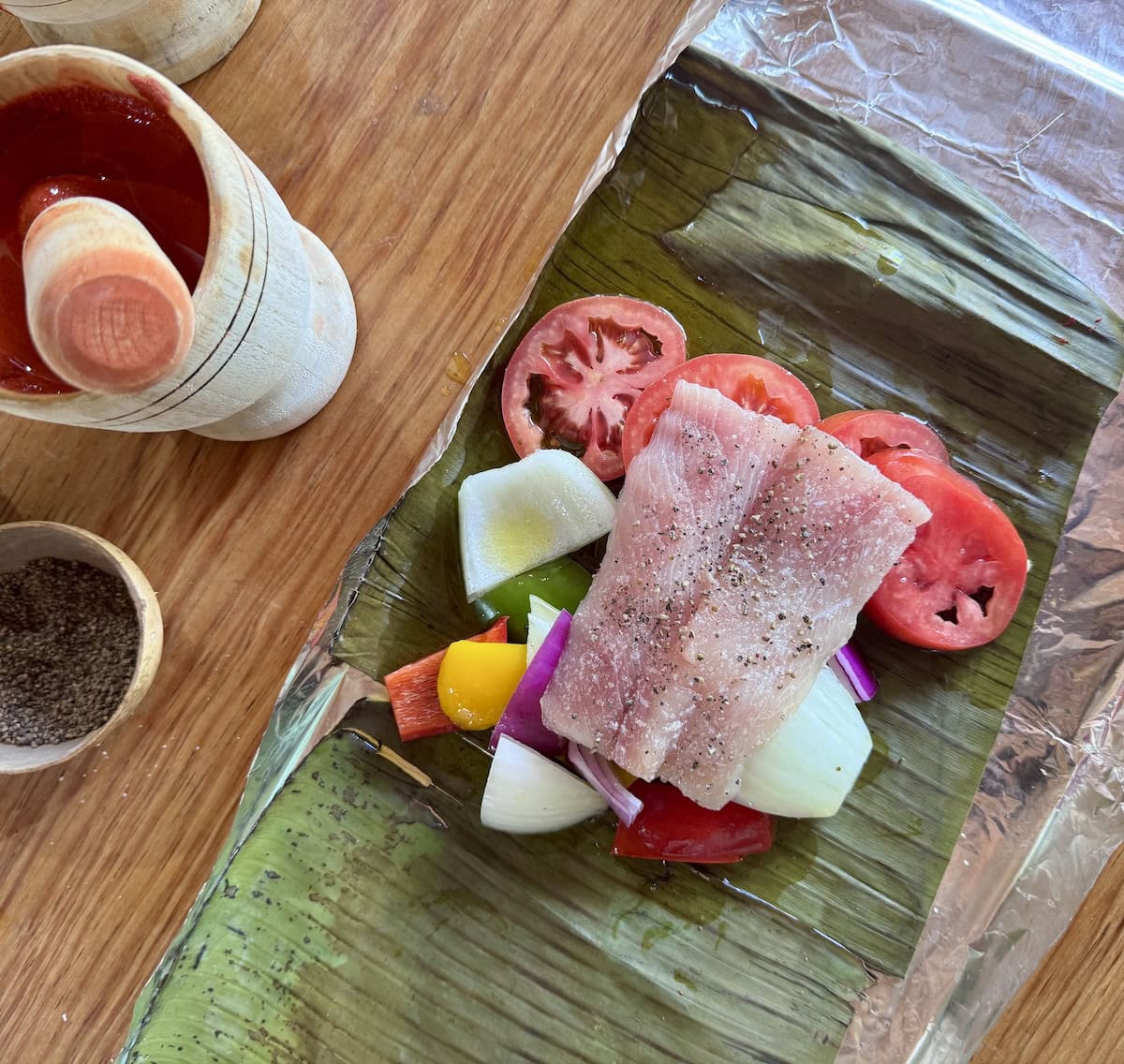 Mahi fish over vegetables on a banana leaf.